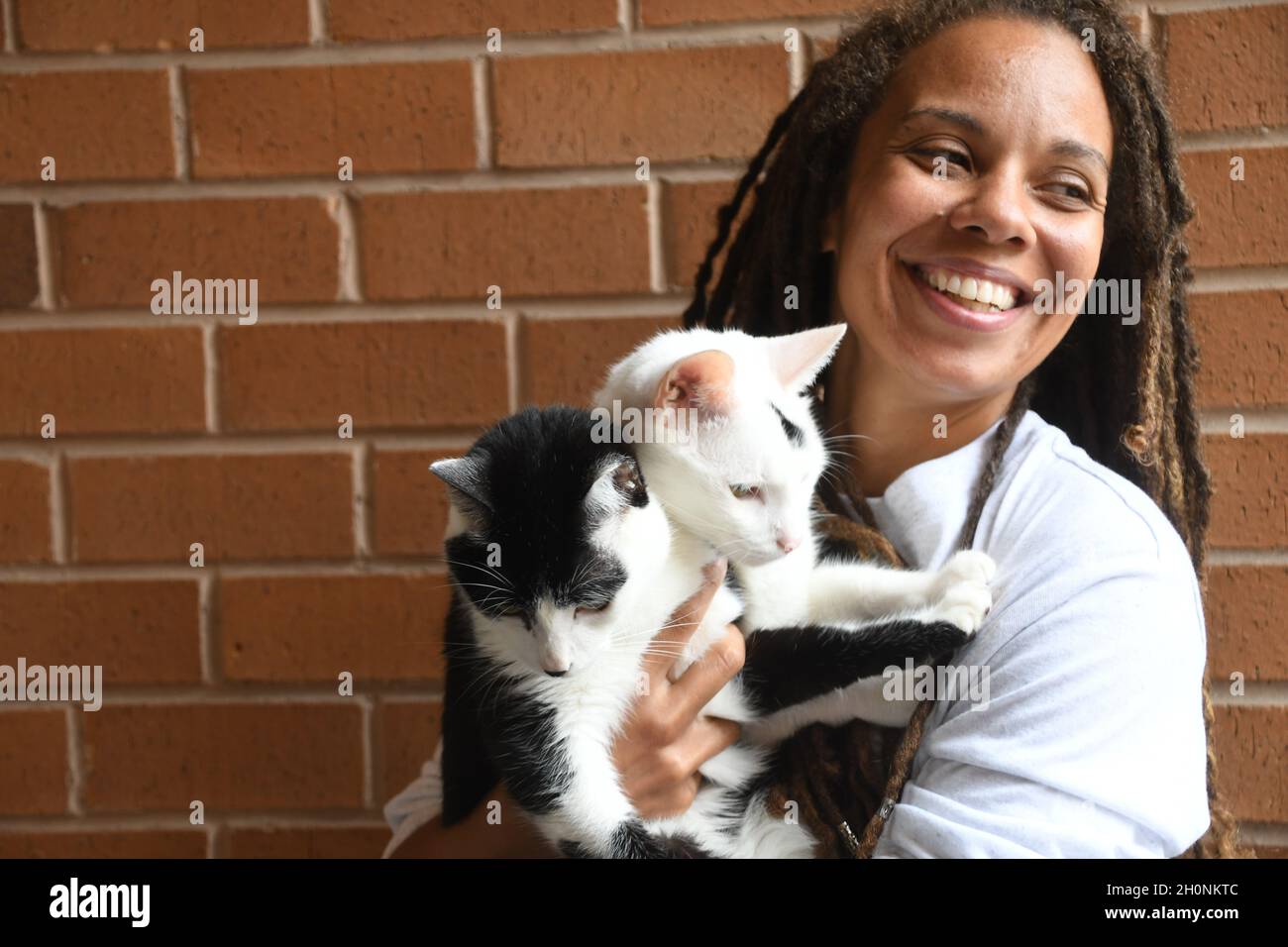 Woman smiles while holding two cats Stock Photo