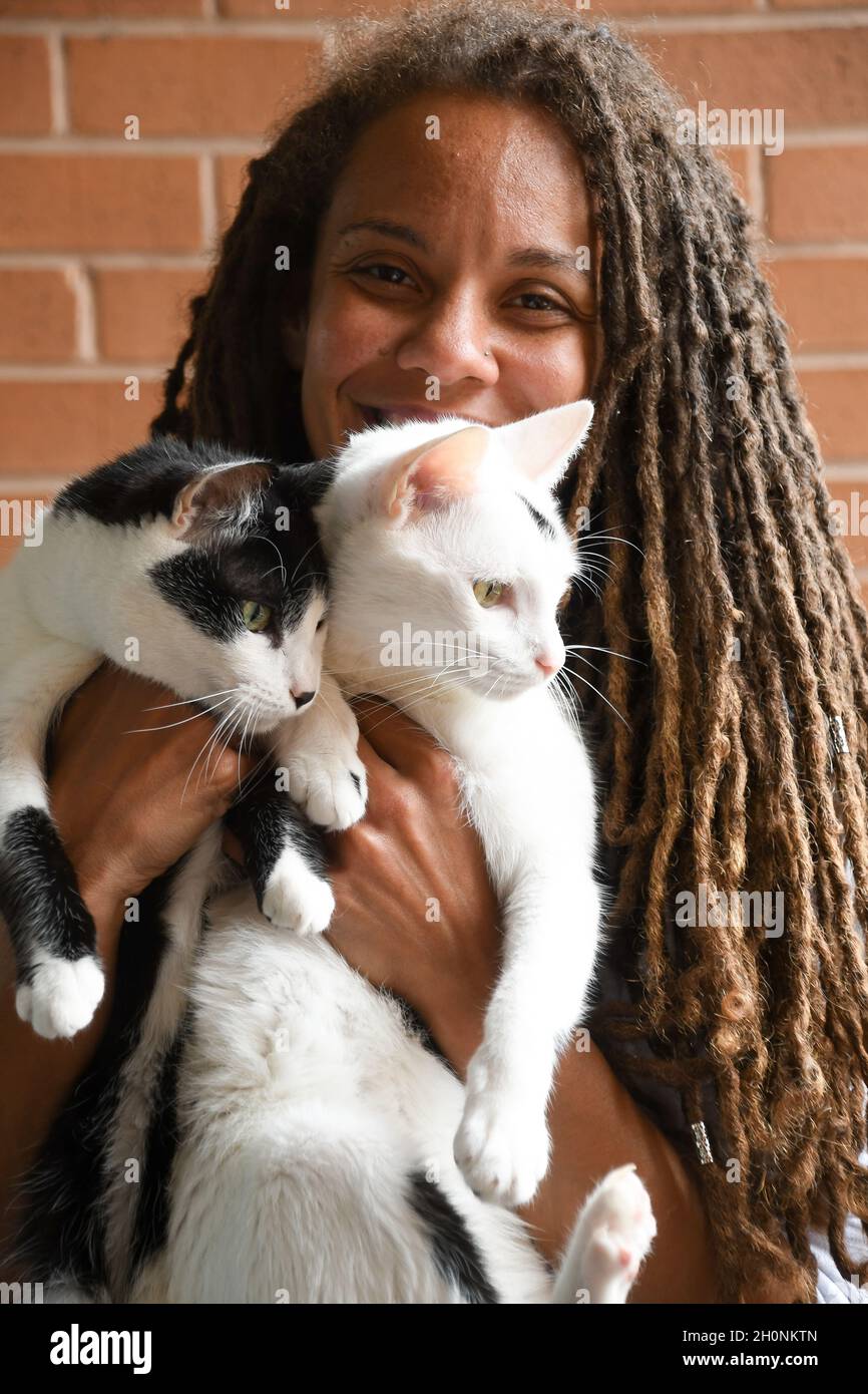 Woman smiles while holding two cats Stock Photo