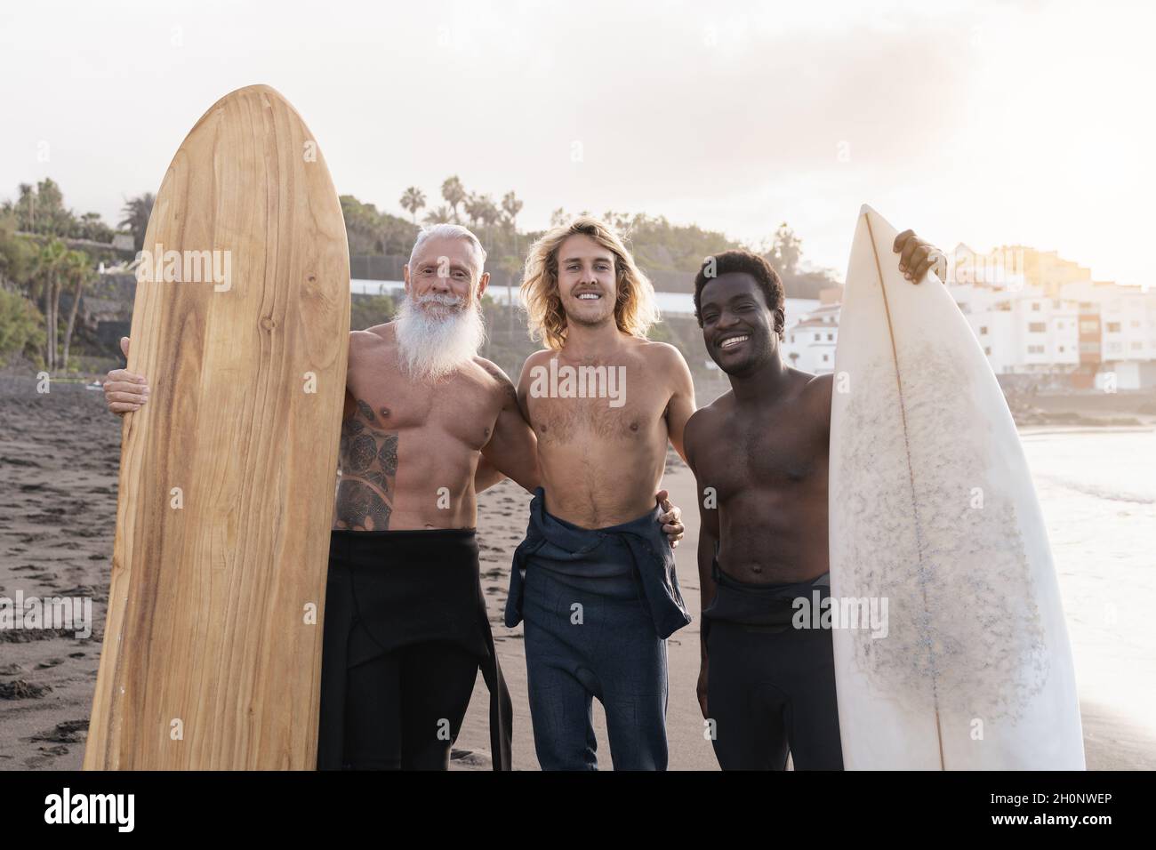 Multiracial surfer friends holding surf boards after extreme water sport session with beach on background - Main focus on senior man face Stock Photo