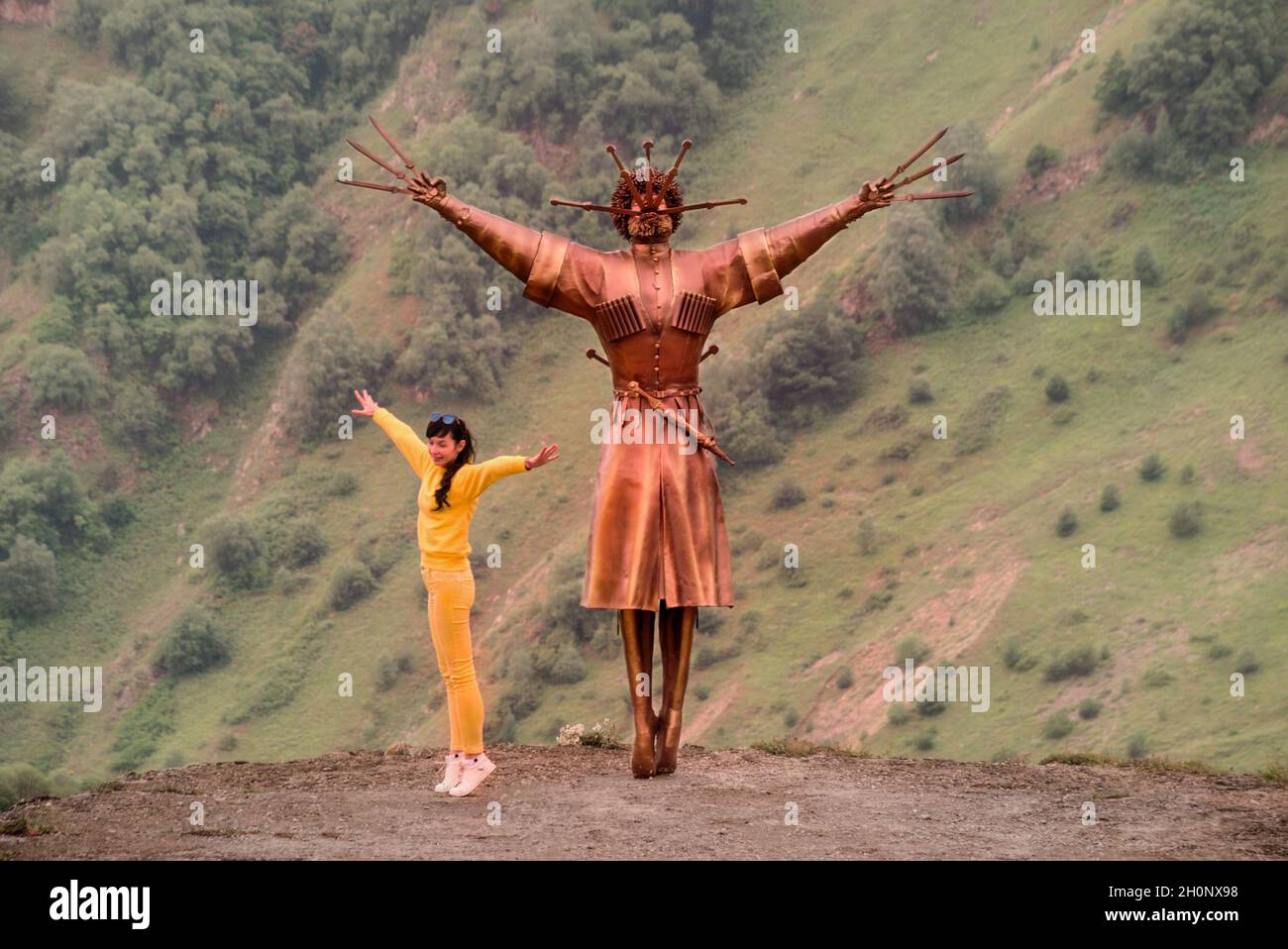 VERKHNIY ZGID, RUSSIA - 07 25 2021: A teenage girl dancing folk Ossetian dace beside the Dance With Daggers monument towering along steep mountain Stock Photo