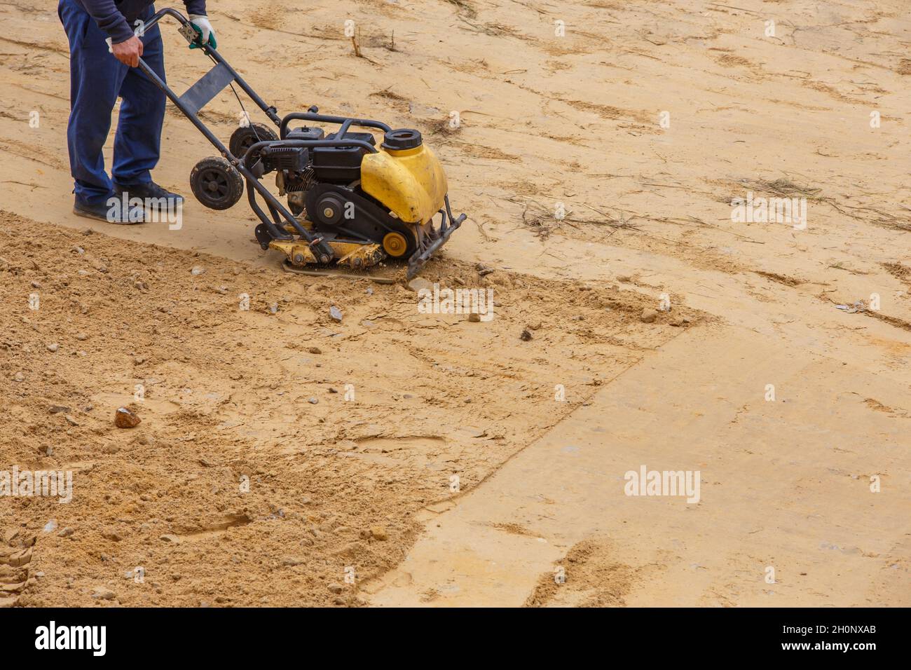 Worker in use vibratory plate compactor for path construction. Plate