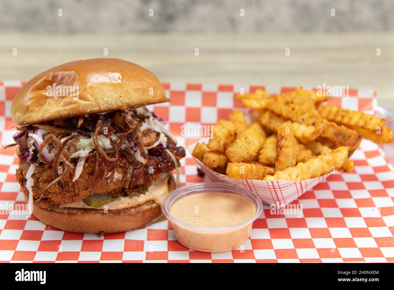 Spicy hot chicken sandwich loaded with onions and pickles topped with cole slaw and served with a dipping sauce. Stock Photo