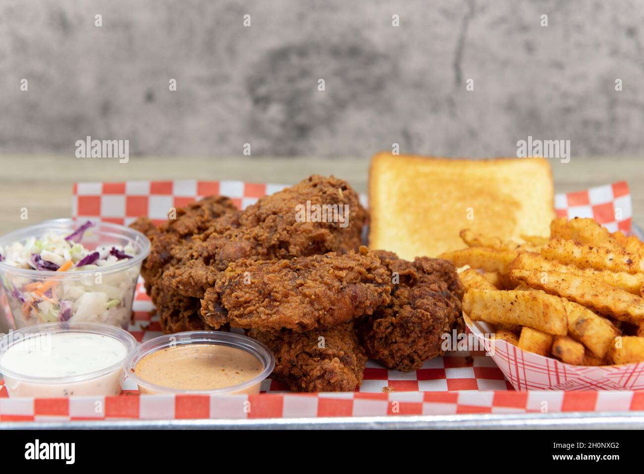 Spicy hot chicken wings piled with french fries, cole slaw, toast, and two dipping sauces Stock