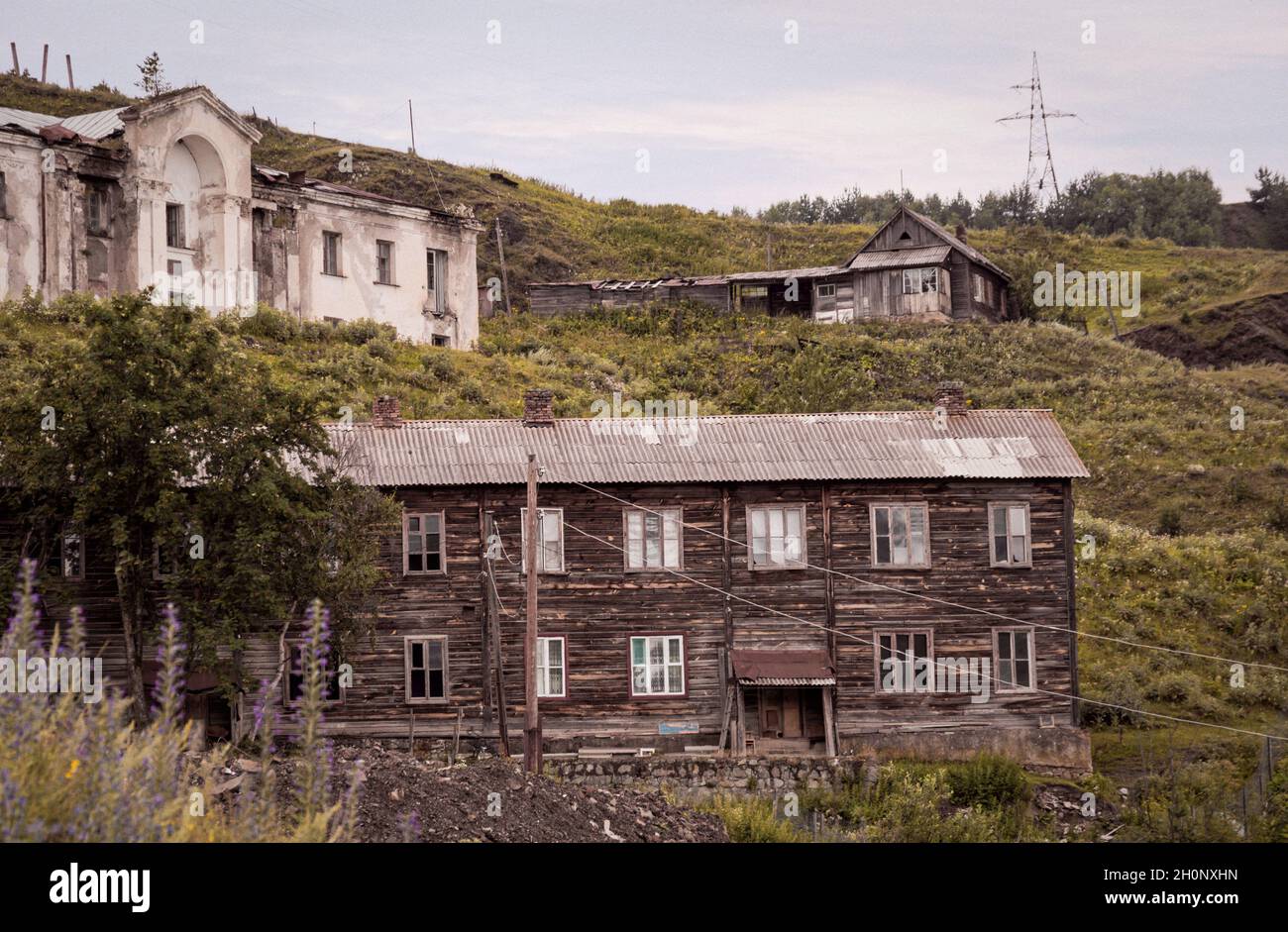 Old abandoned wooden two storey building in deserted old town or village on the slope of the hill surrounded wit similarly semi-ruined houses Stock Photo