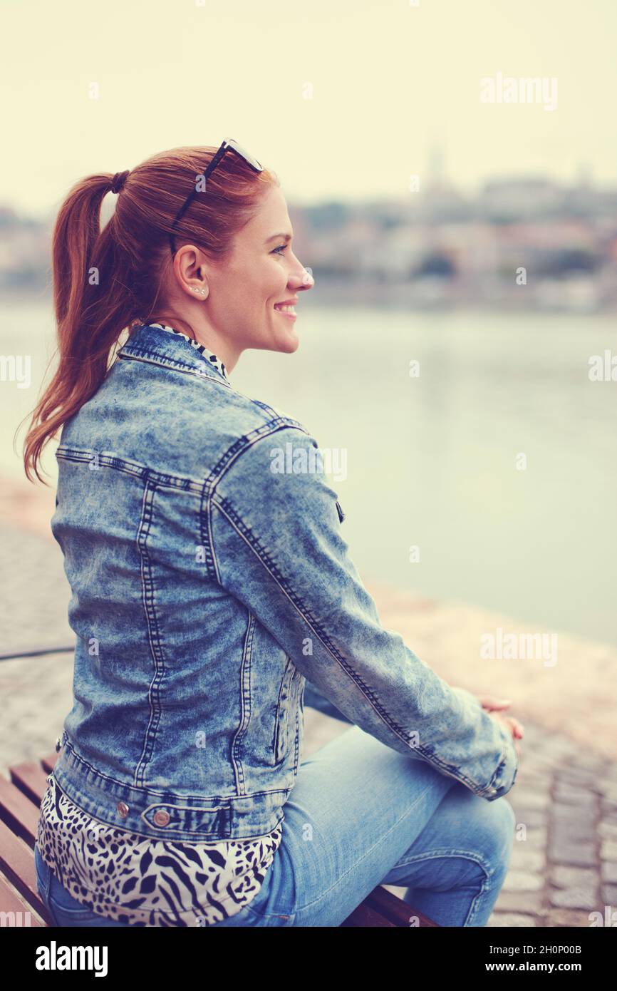 Young redhead urban Caucasian woman looking away at city riverbank, depth of field, profile view, Budapest, Hungary Stock Photo