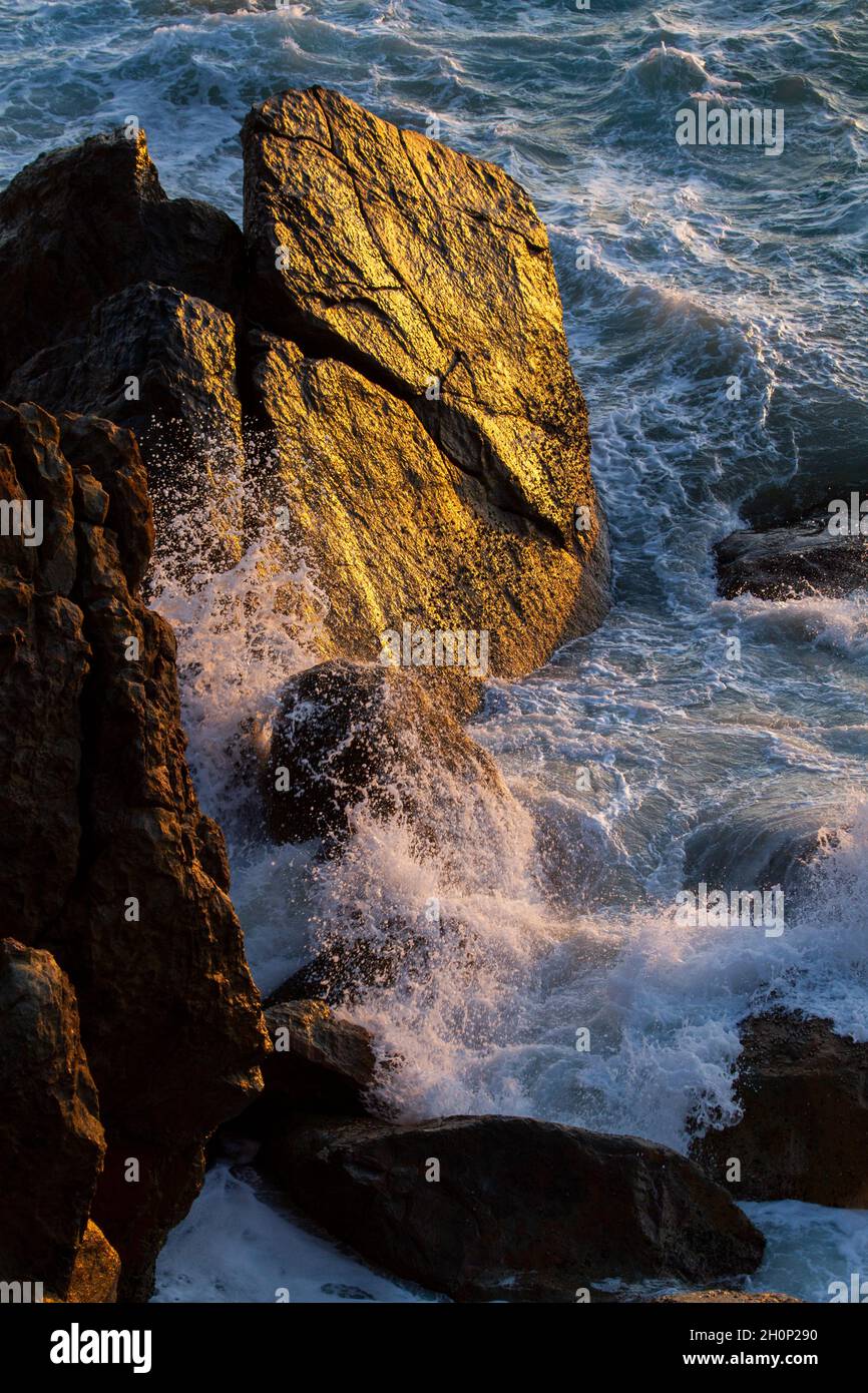 Morning light shines on boulders as waves crash against them. Stock Photo