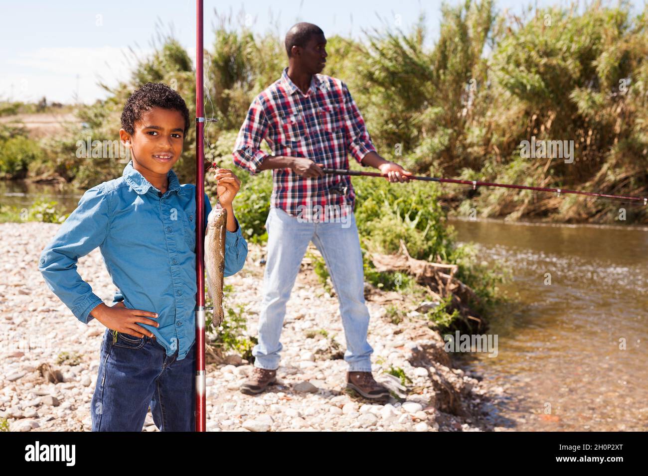 Man and boy holding fish on rod Stock Photo