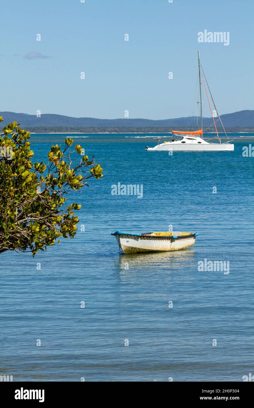 Row boat dinghy and a cruising catamaran yacht anchored in an estuary.. Stock Photo