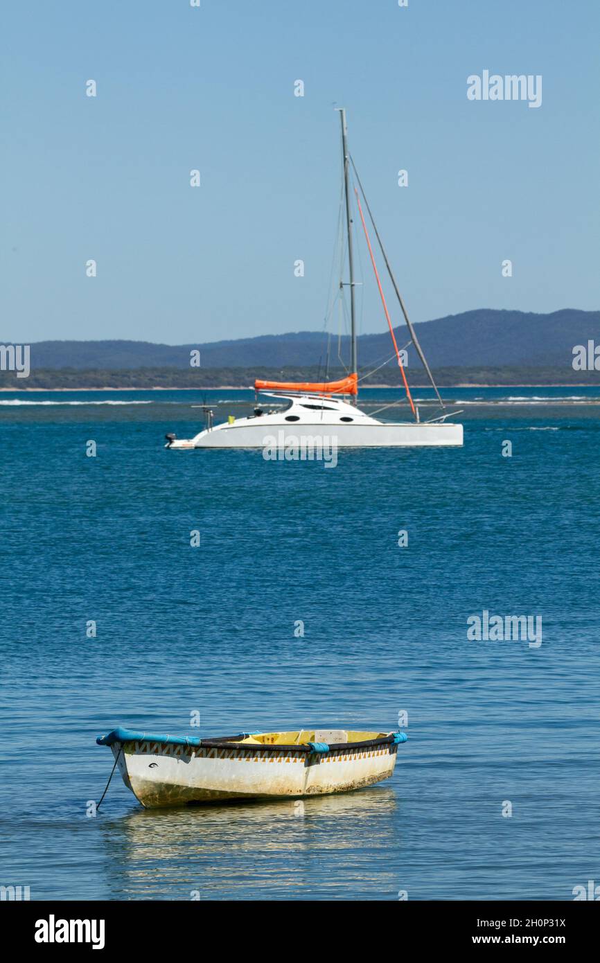Row boat dinghy and a cruising catamaran yacht anchored in an estuary.. Stock Photo