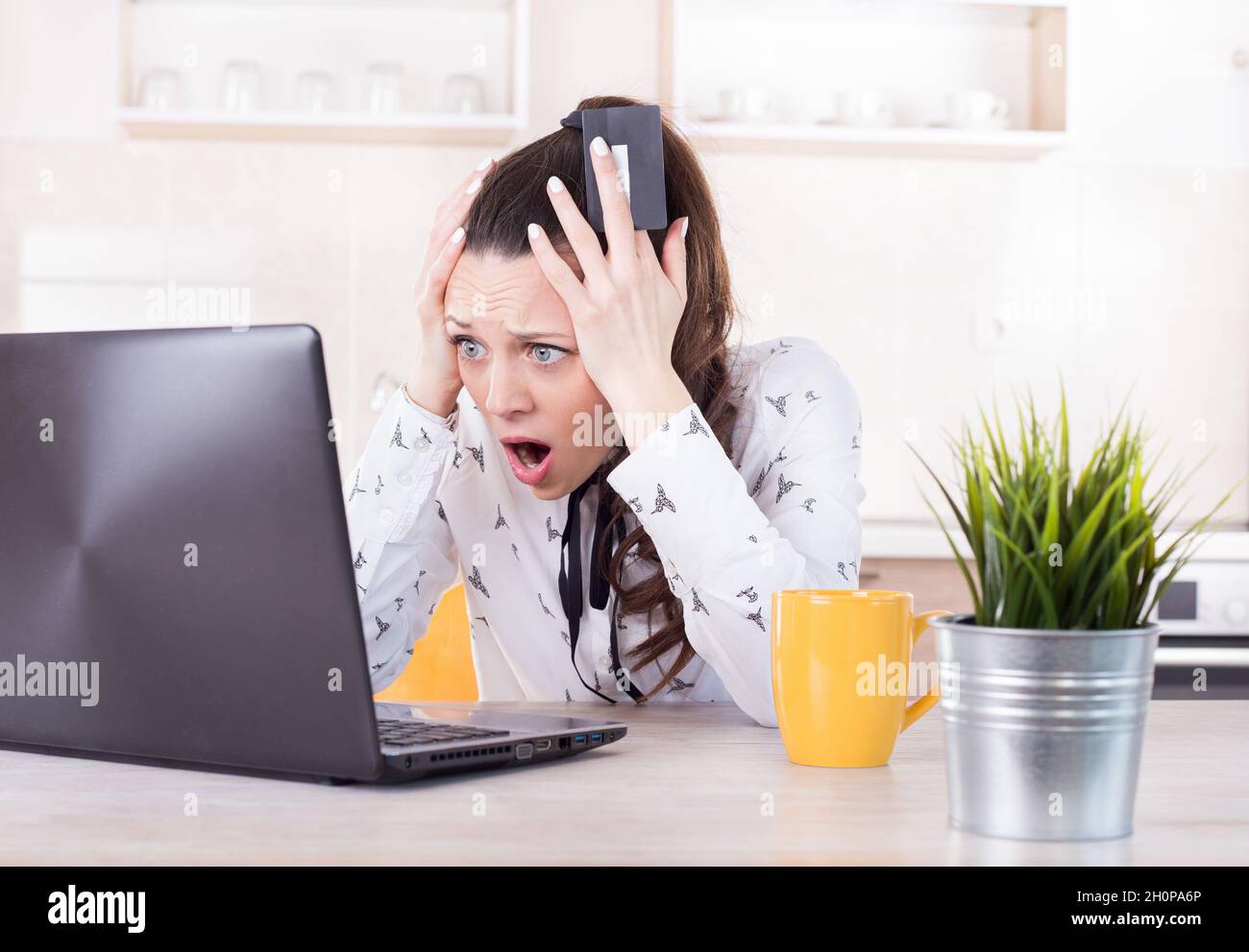 Shocked young woman holding credit card and looking at laptop. Negative surprise in e-banking Stock Photo