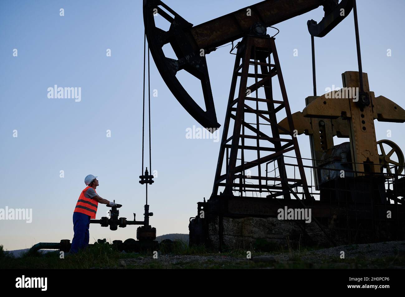 Petroleum operator in work vest using pumping unit to extract crude oil
