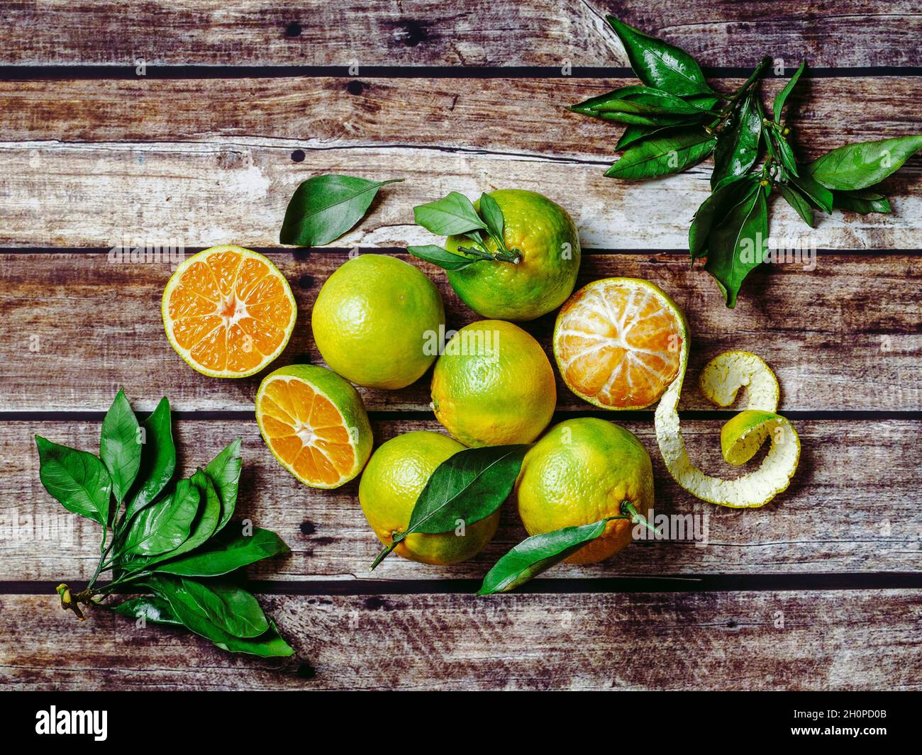 Green mandarines on old wooden background. Fresh ripe half, whole and peeled green tangerines with leaves, top view or flat lay Stock Photo