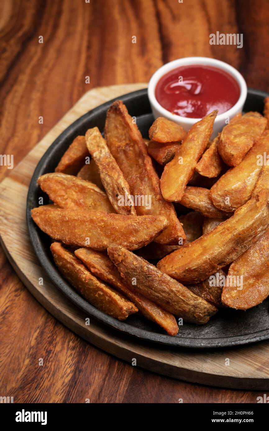 spicy curry powder coated crispy deep fried potato wedges on wood table background Stock Photo