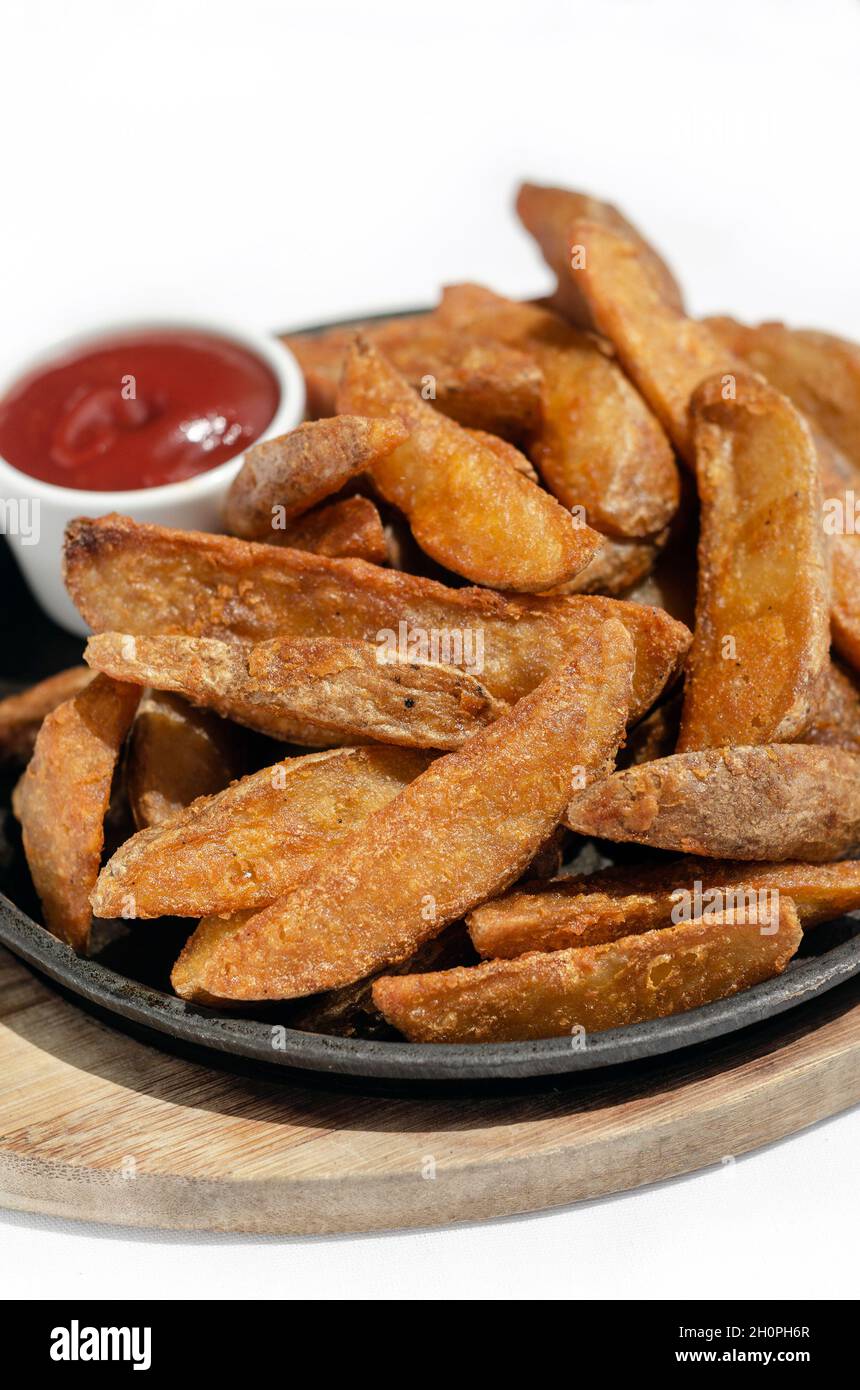 spicy curry powder coated crispy deep fried potato wedges on plate with white background Stock Photo