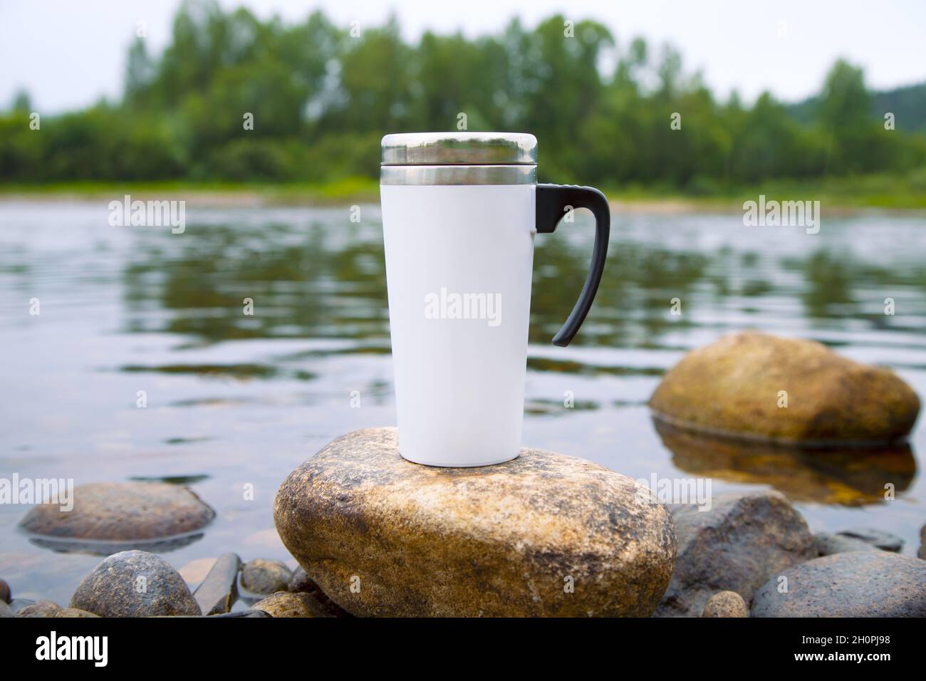 White travel coffee mug mockup with river view. Empty mug mock up for design promotion. Stock Photo