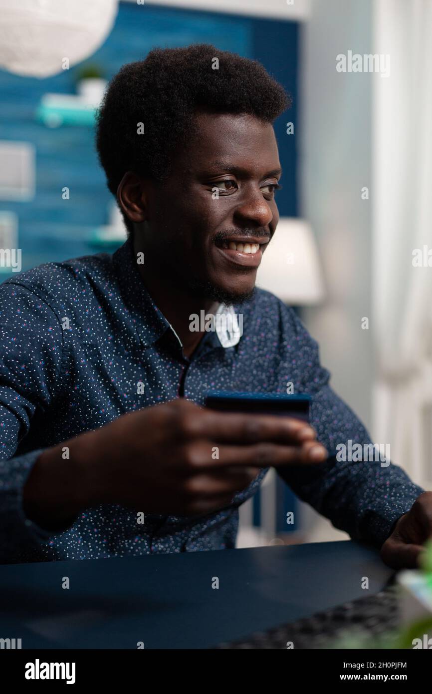 Teenager consumer making online shopping on retail store paying order with credit card. Man sitting at desk in living room doing online payment with electronic money using computer Stock Photo