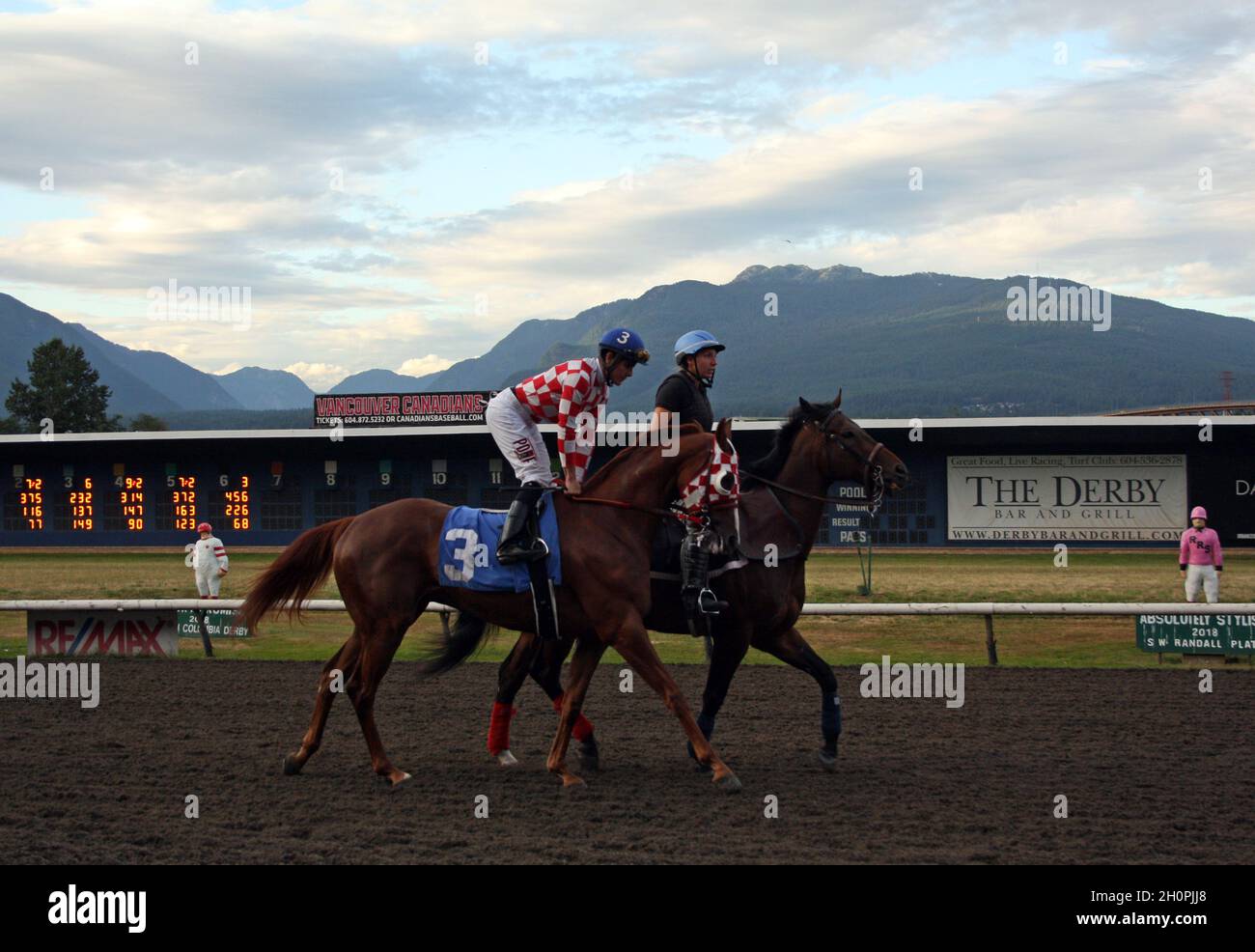 VANCOUVER, CANADA - Jul 26, 2021: A shot of a woman and a man on horses at the famous Hastings Racecourse in Vancouver, Canada with hills in the backg Stock Photo