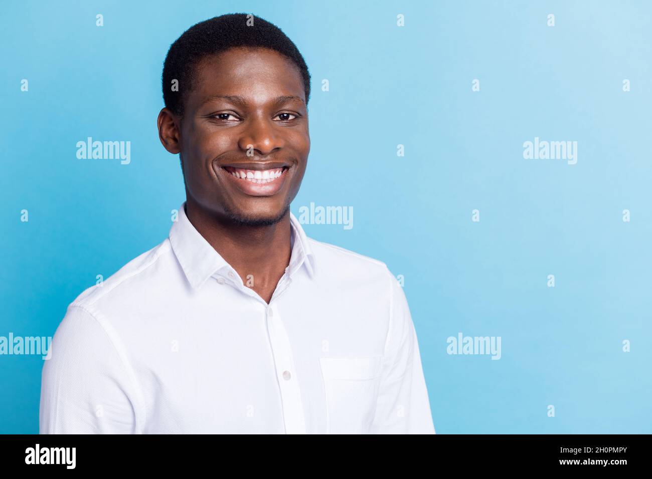 Photo of cute pretty dark skin man wear white shirt empty space smiling isolated blue color background Stock Photo