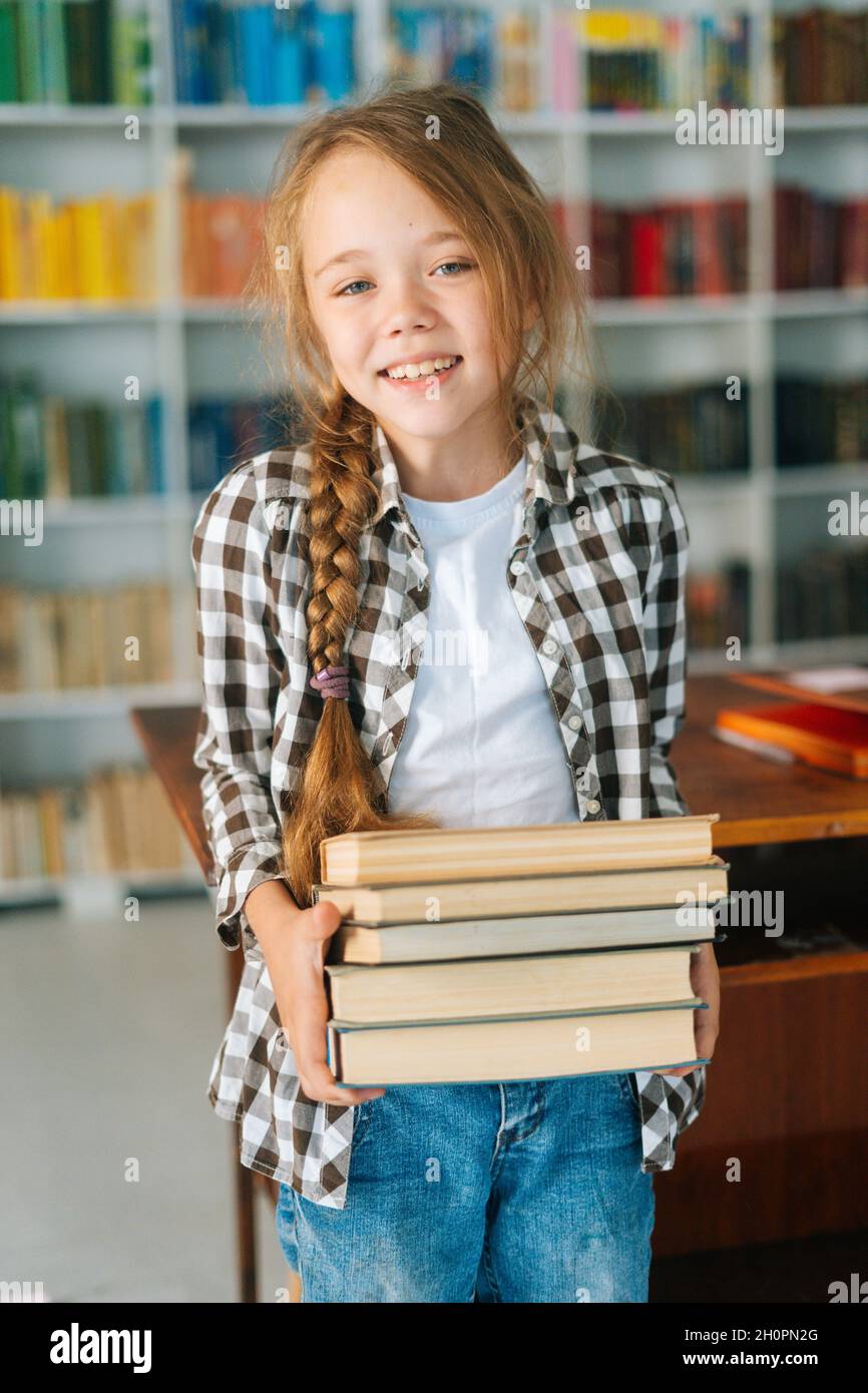 Vertical portrait of smiling elementary child school girl holding stack ...