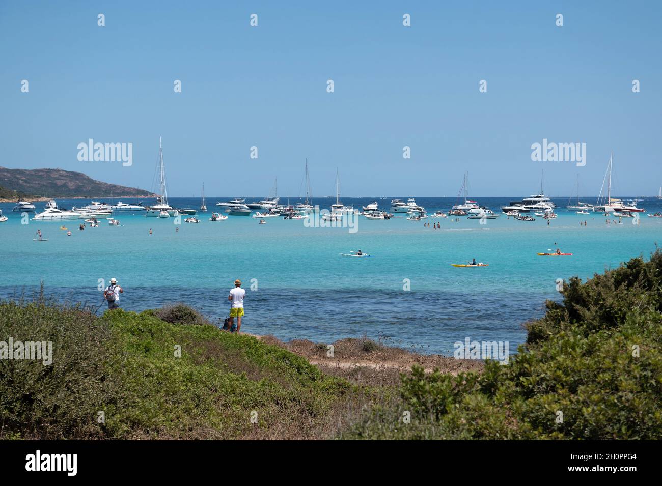 Corse du Sud department (southern Corsica): two hikers on the coastal path facing the sea with boats and sailboats near Piantarella Beach, lagoon of P Stock Photo