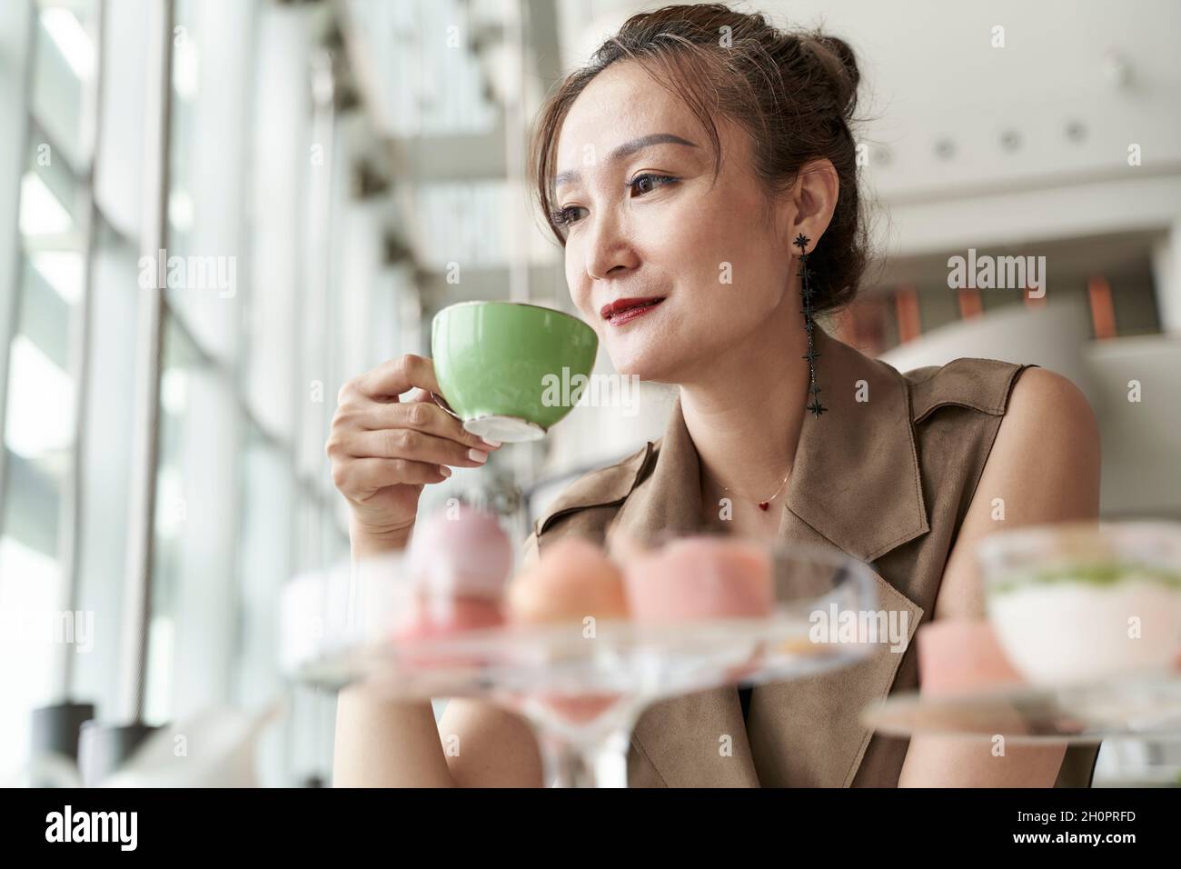 mature asian woman sitting at table having afternoon tea in coffee shop of luxurious hotel Stock Photo
