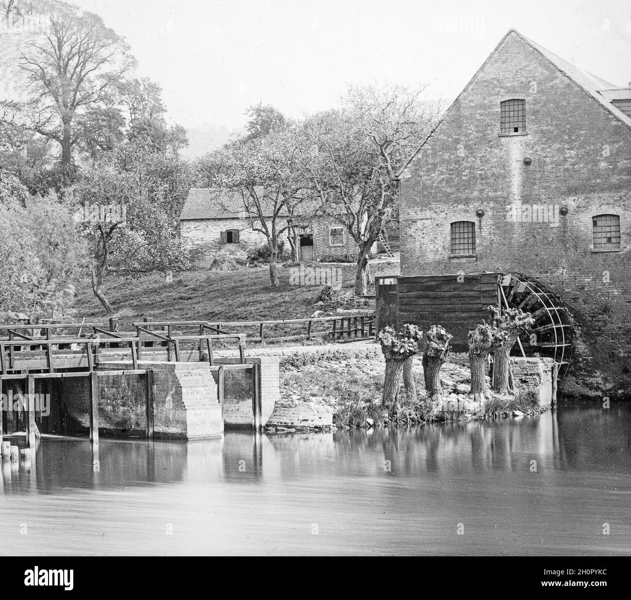 Late Victorian black and white photograph showing a water mill with water wheel in a small village in England. Stock Photo