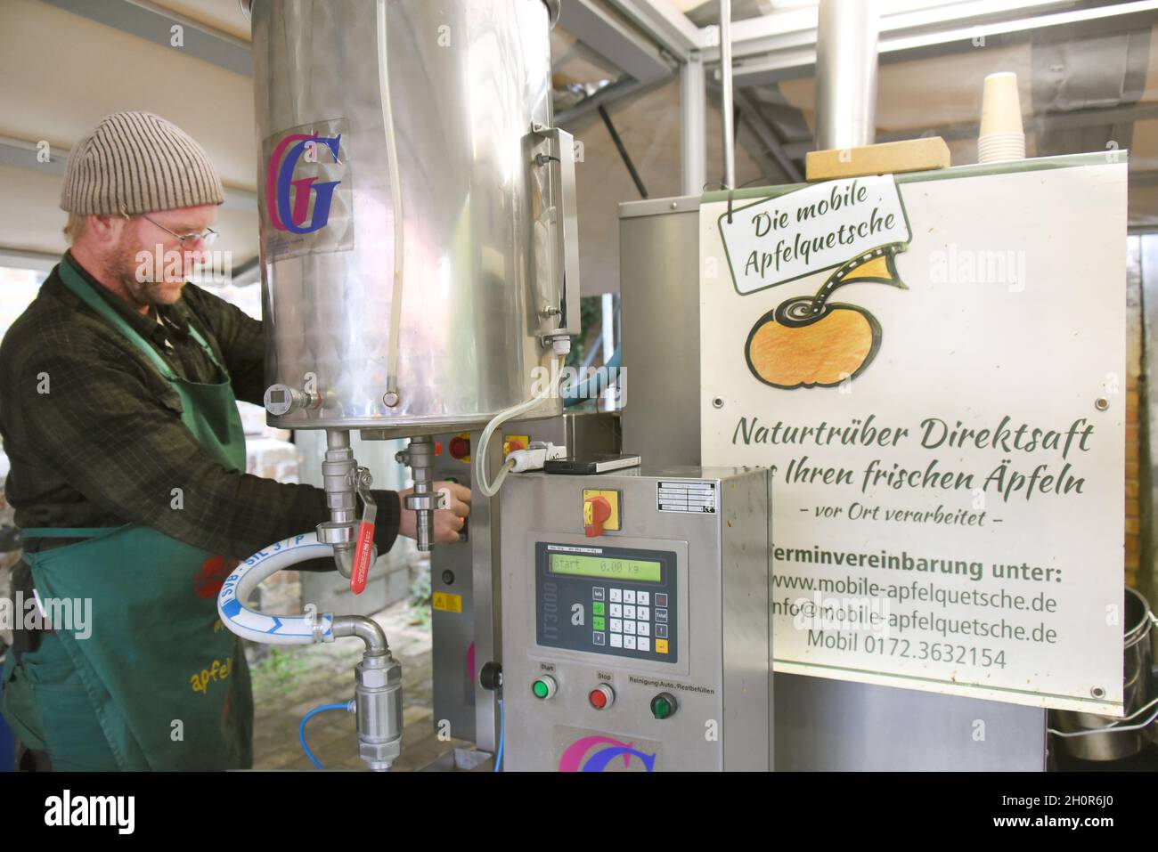 11 October 2021, Saxony, Fuchshain Bei Leipzig: The Leipzig garden and landscape builder Andreas Richter (r), who has set up his mobile apple crusher for one day on a farm in Fuchshain, checks freshly squeezed apple juice from fruit brought by his customers. In front of the eyes of his customers, the small fruit factory on wheels will be processing the vitamin-rich fruit into naturally cloudy direct juice in various locations until the end of October and can then be taken home in 5-liter packages. With the mobile cidery, Andreas Richter wants to contribute to the preservation, but also to the Stock Photo