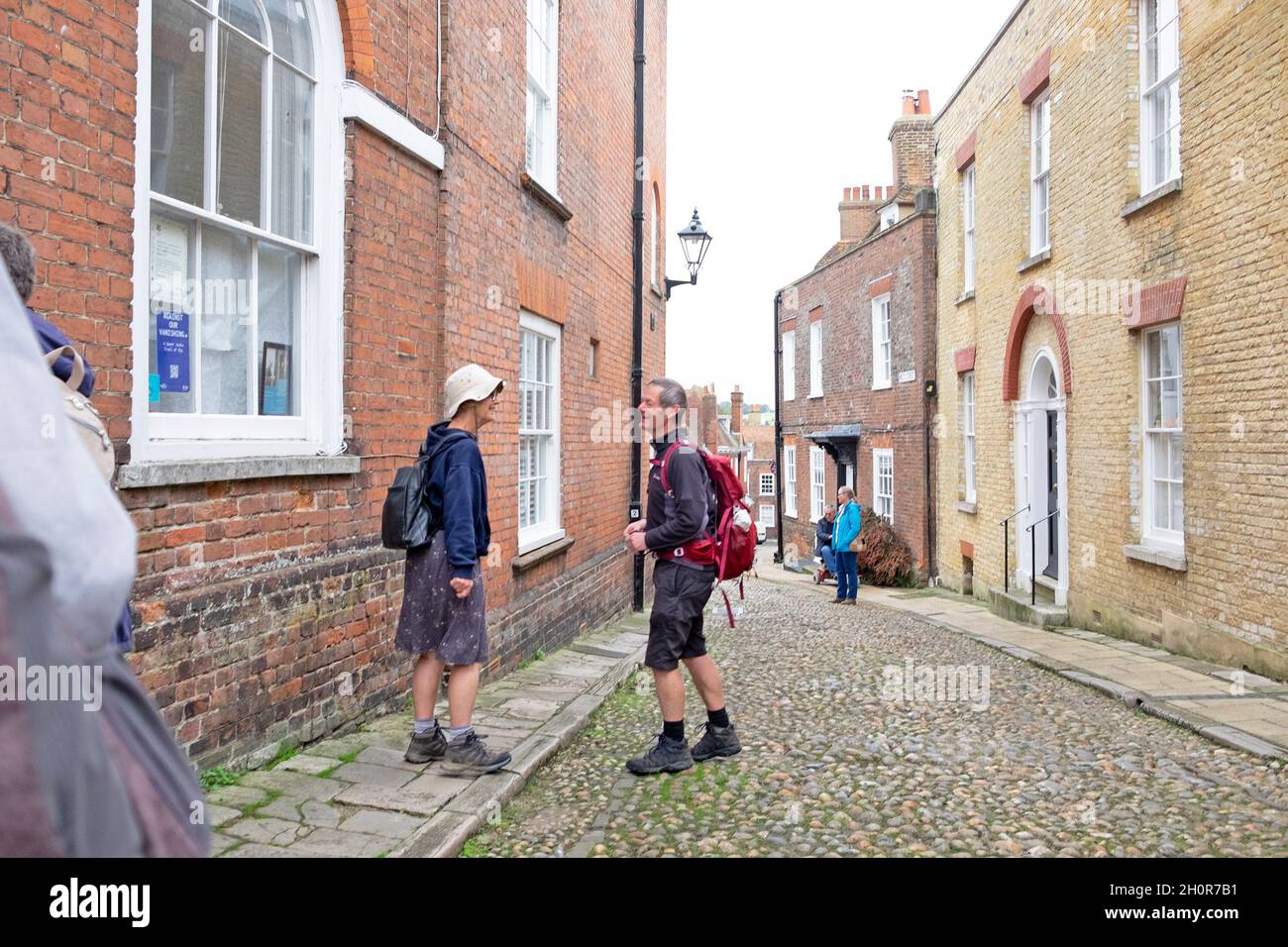 Two older people couple walkers hikers wearing backpacks rucksacks standing talking in street Rye East Sussex England Great Britain UK KATHY DEWITT Stock Photo