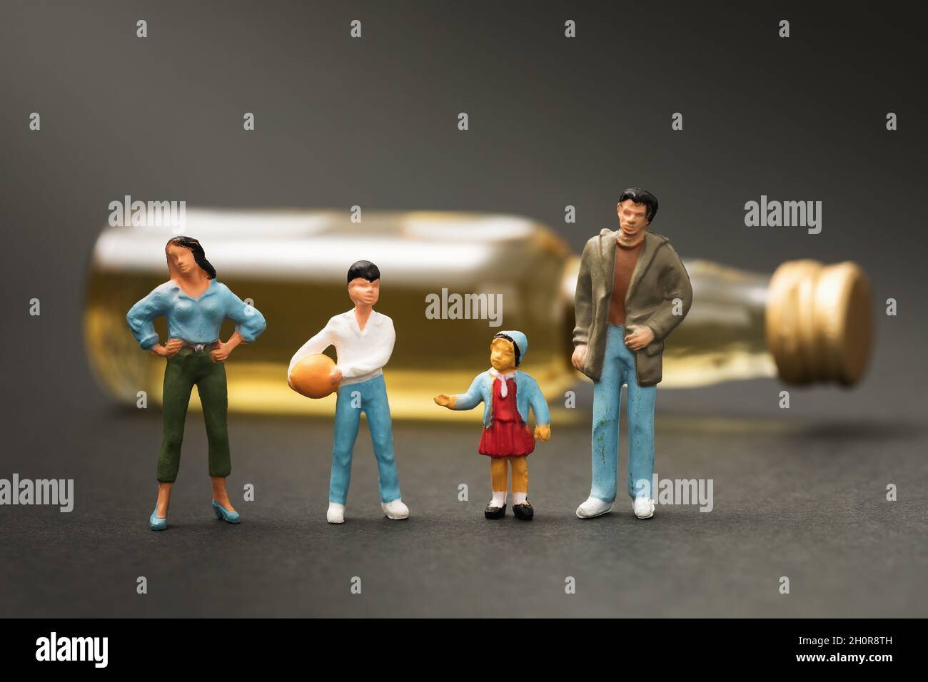 Toy men made of plastic on the background of a lying bottle of whiskey, a concept on the topic of a threat to the family due to alcohol abuse Stock Photo