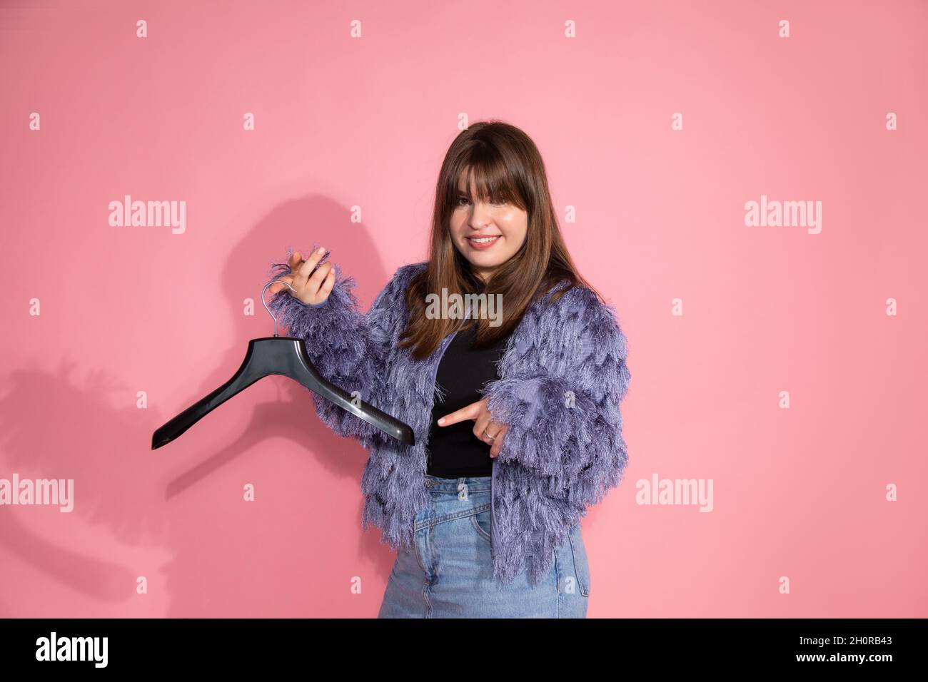 Blogger teaches classes on creating stylish image. A young pretty woman holds empty clothes hanger on pink background in studio. Stock Photo