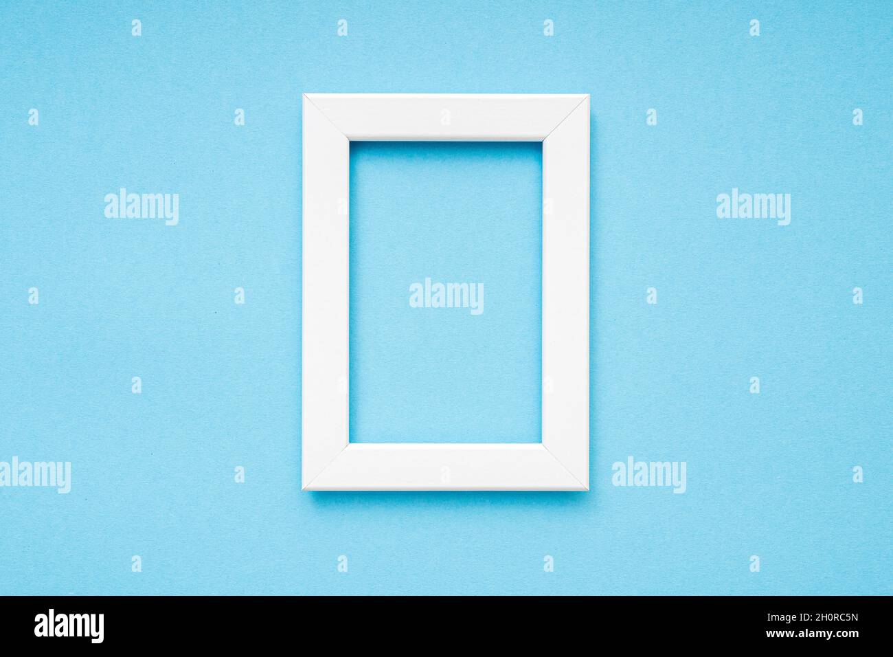 White wooden photo frame on blue surface, minimal composition, Vertical photo frame, space for text, top view Stock Photo