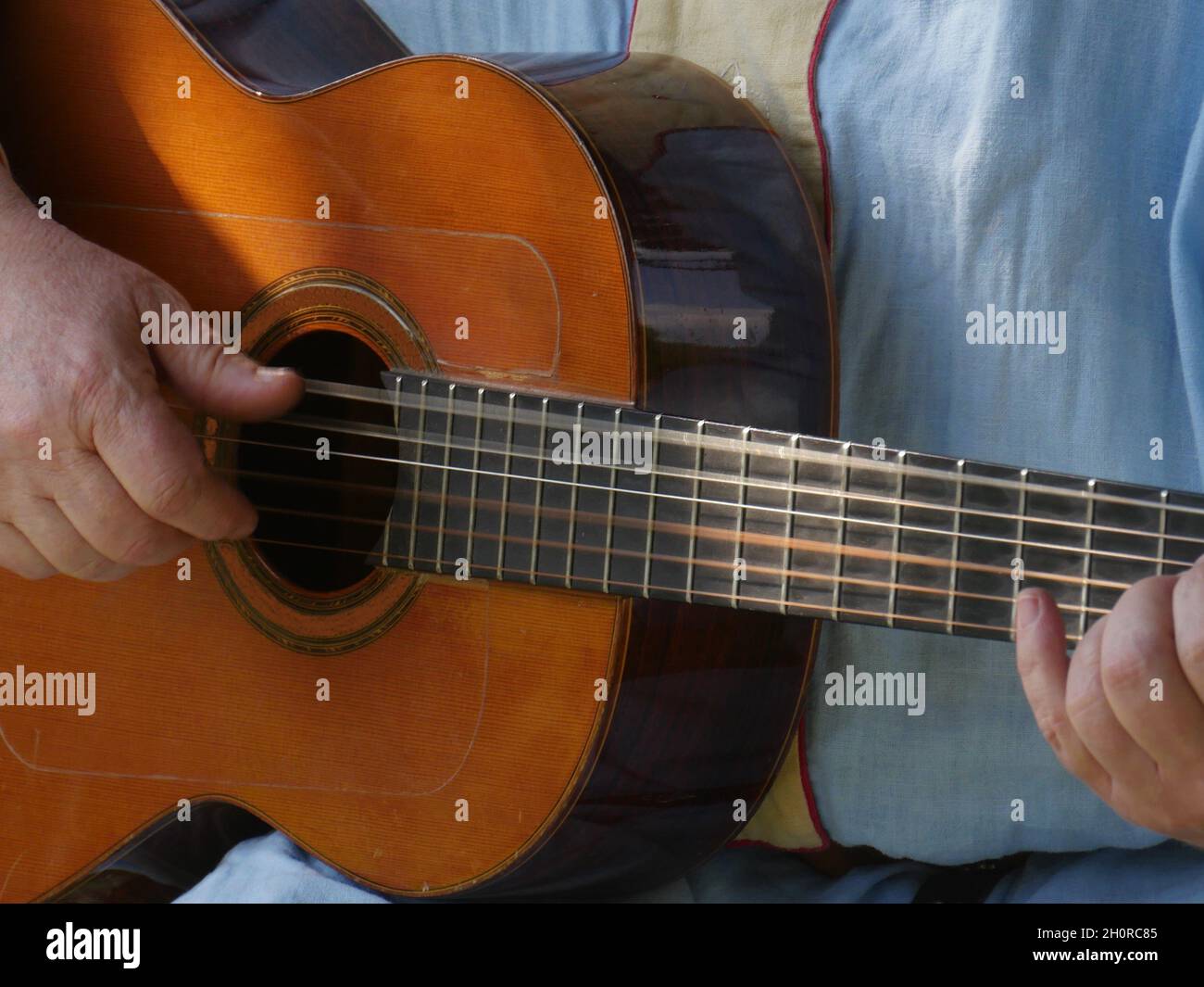 Partial view of a straight hands played wooden trekking guitar, strings swinging, arm laid on to play a chord Stock Photo