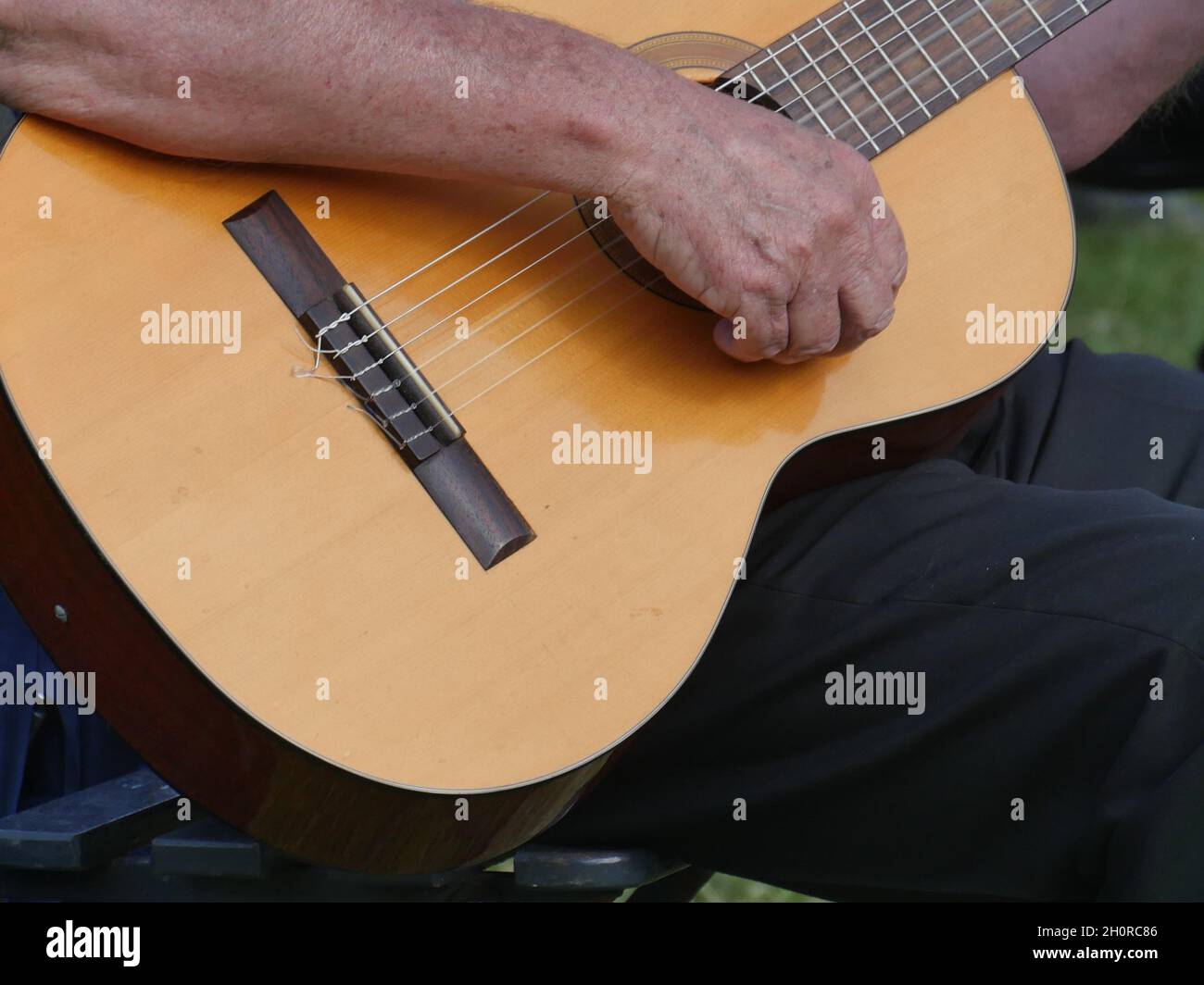 Partial view of a straight played wooden trekking guitar, strings swinging, arm laid on to play a chord Stock Photo