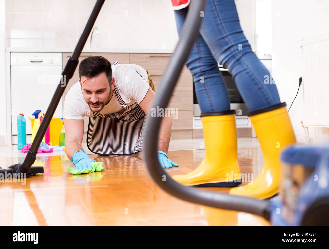 Young couple doing chores together. Man wiping floor on knees and girl