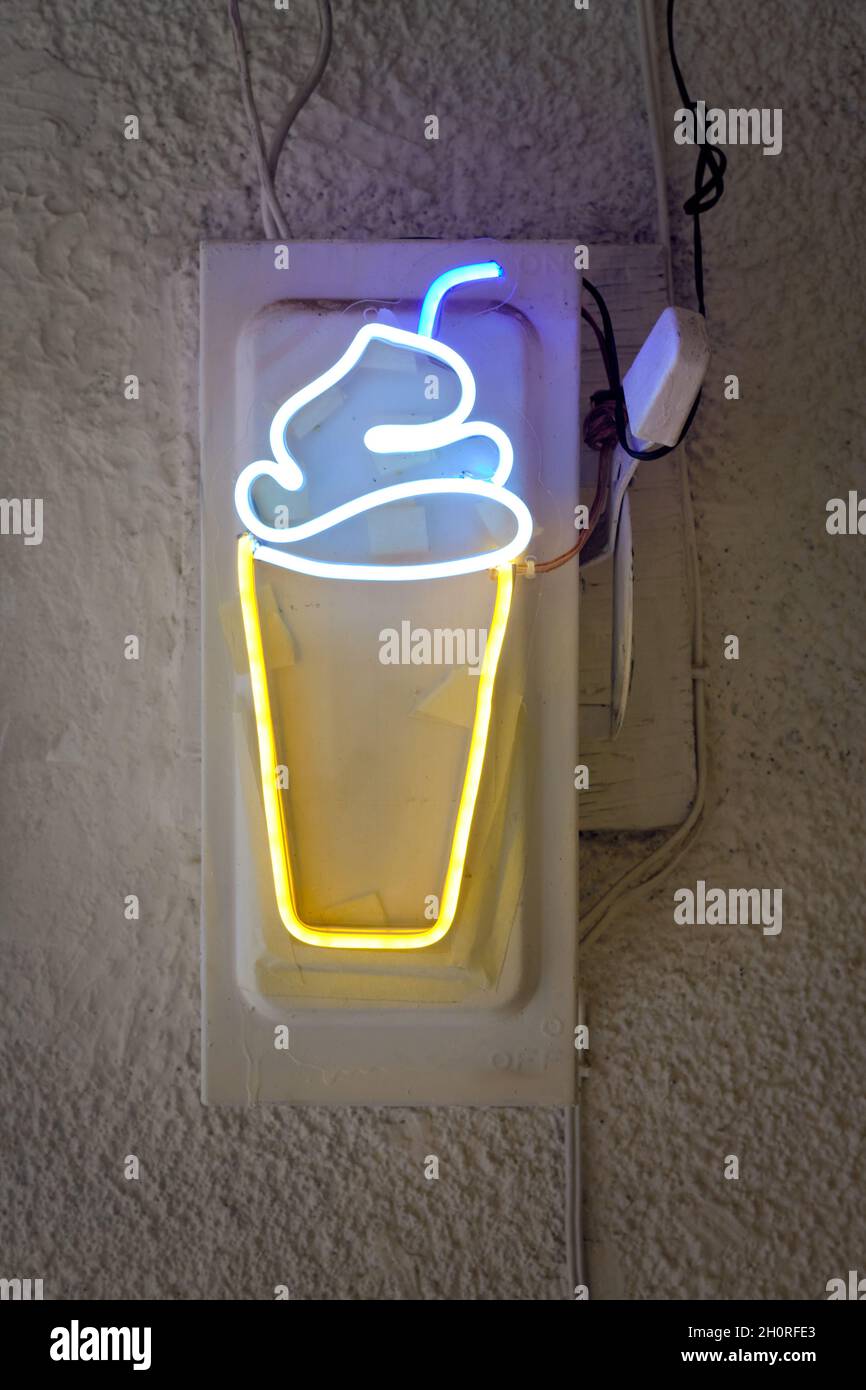 Yellow and blue neon sign on a wall, in the shape of a milk-shake with a straw. Stock Photo