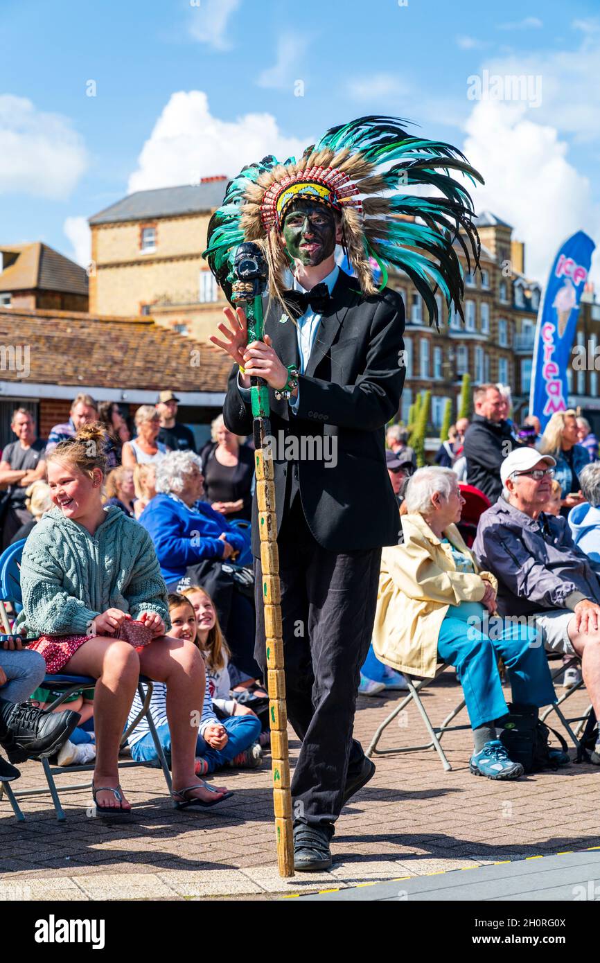 Man standing in black suit, bowtie and wearing an indian feather bonnet smiling at viewer. The fool from Brooms Bricks and Bowlers morris side. Stock Photo