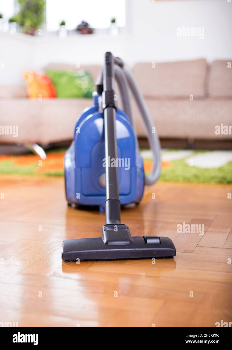 Blue vacuum cleaner standing on parquet floor in front of sofa in living room Stock Photo Alamy