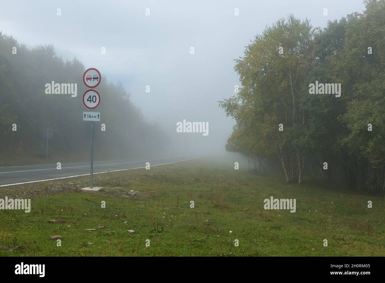 Dangerous fog on the road in the mountains, speed limit road sign Stock Photo