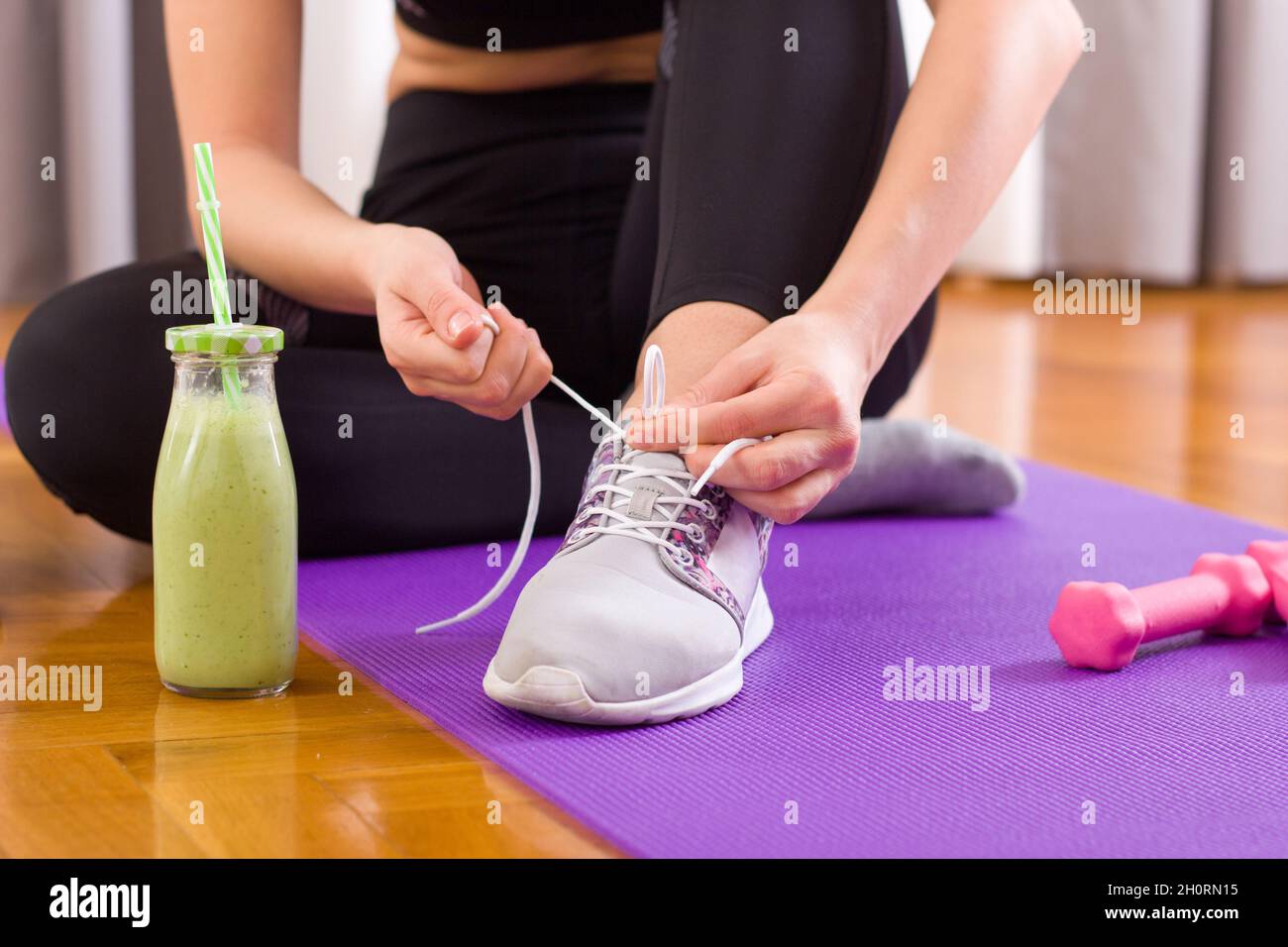 Image showcasing Attractive young woman sitting on yoga mat on parquet floor and tying ...