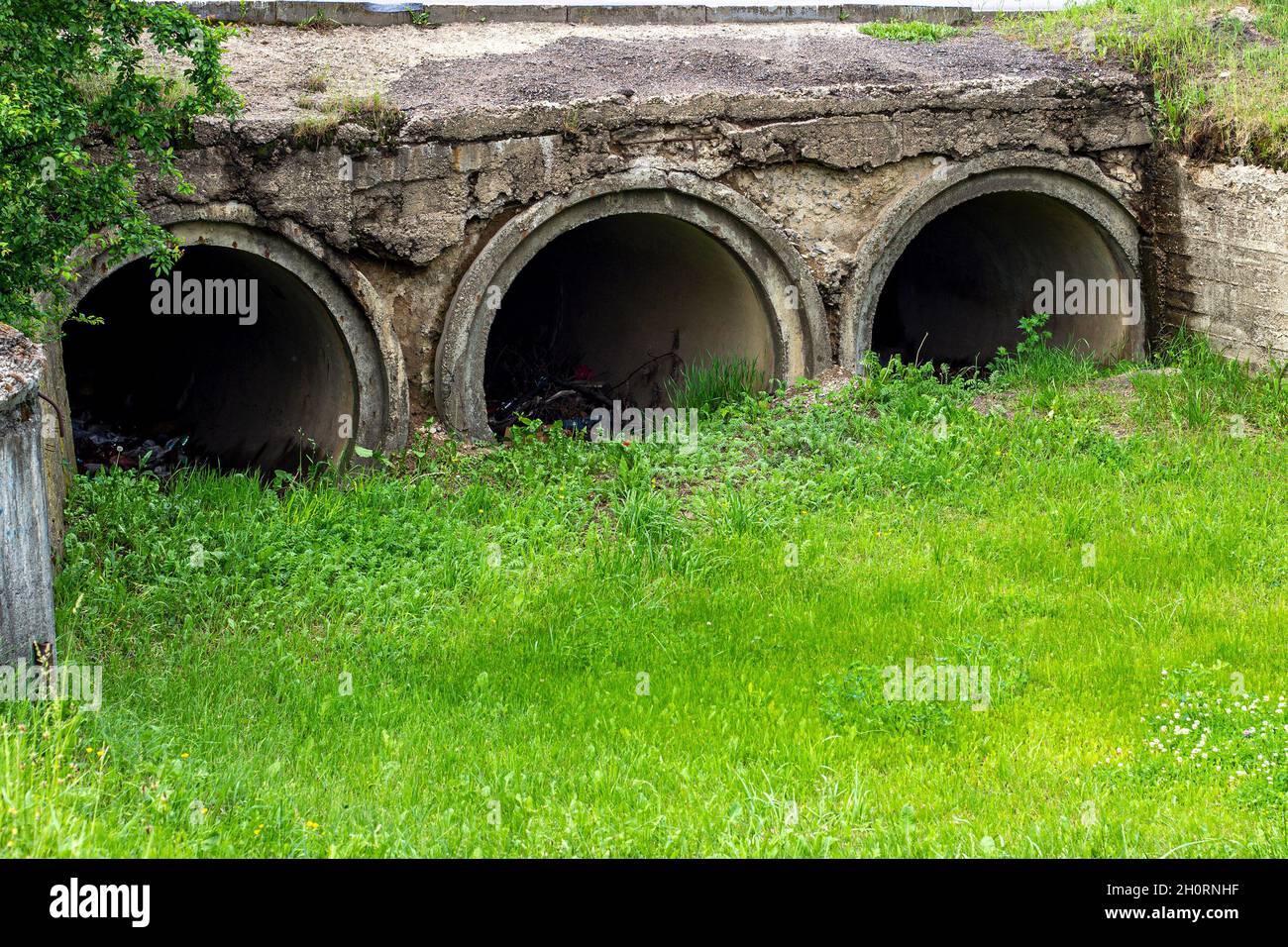 Big sewage drain pipe or effluent release wastewater into the sewage canal with green grass and litter around. Stock Photo