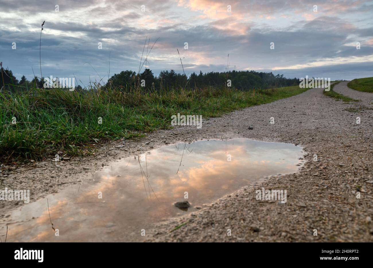 Reflections of a sunset sky in a rain puddle on a gravel road in rural landscape. Seen in Germany in October Stock Photo