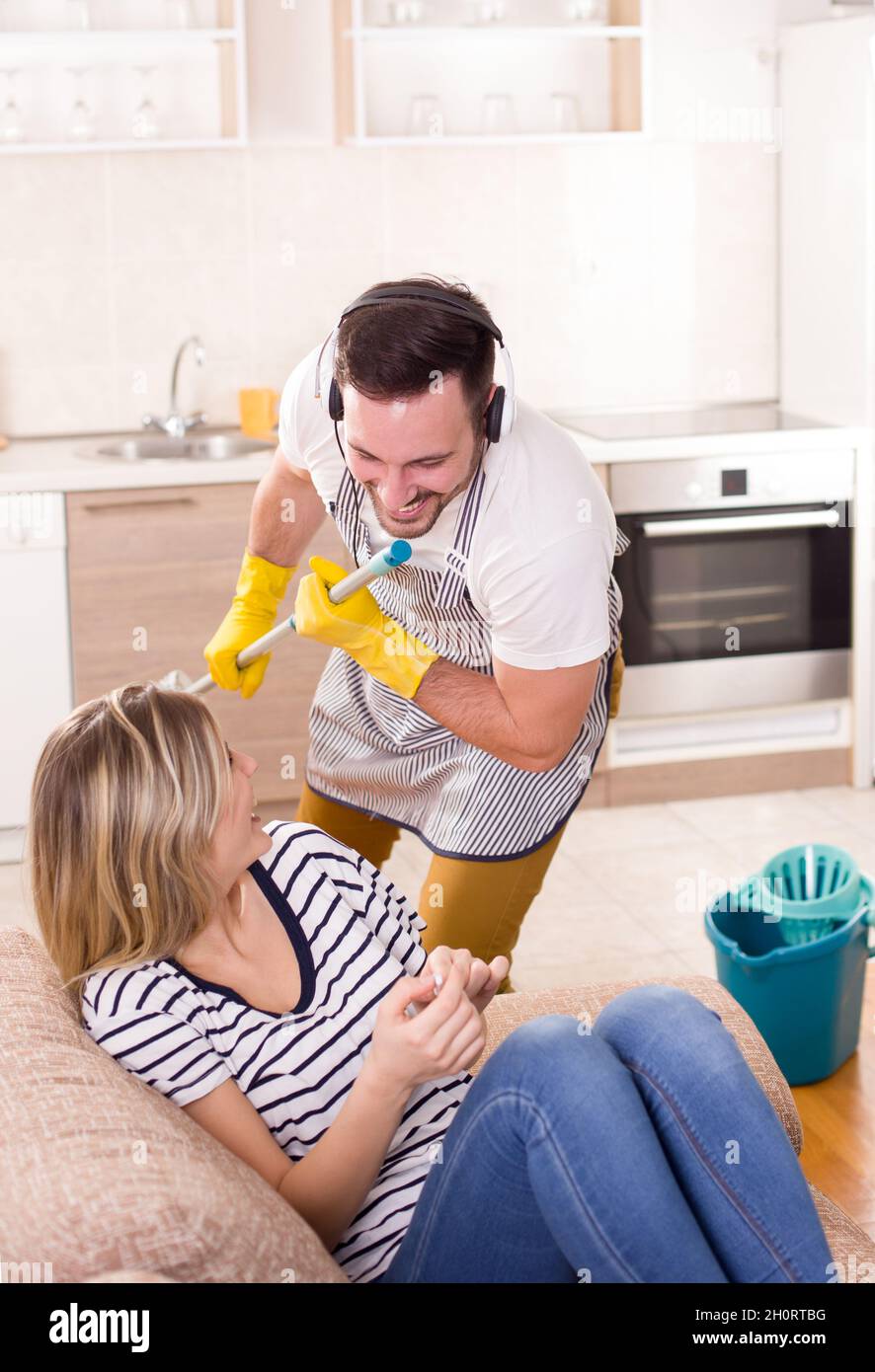 Beautiful young woman resting while man mopping floor and singing