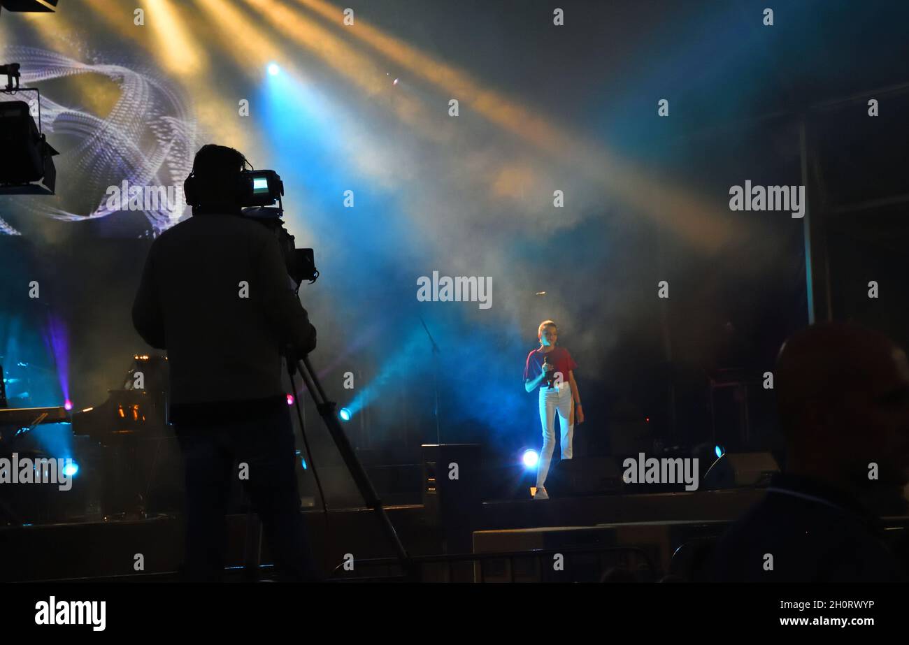 Singer being filmed with light show camera man and camera in view outdoor free event.. Stock Photo