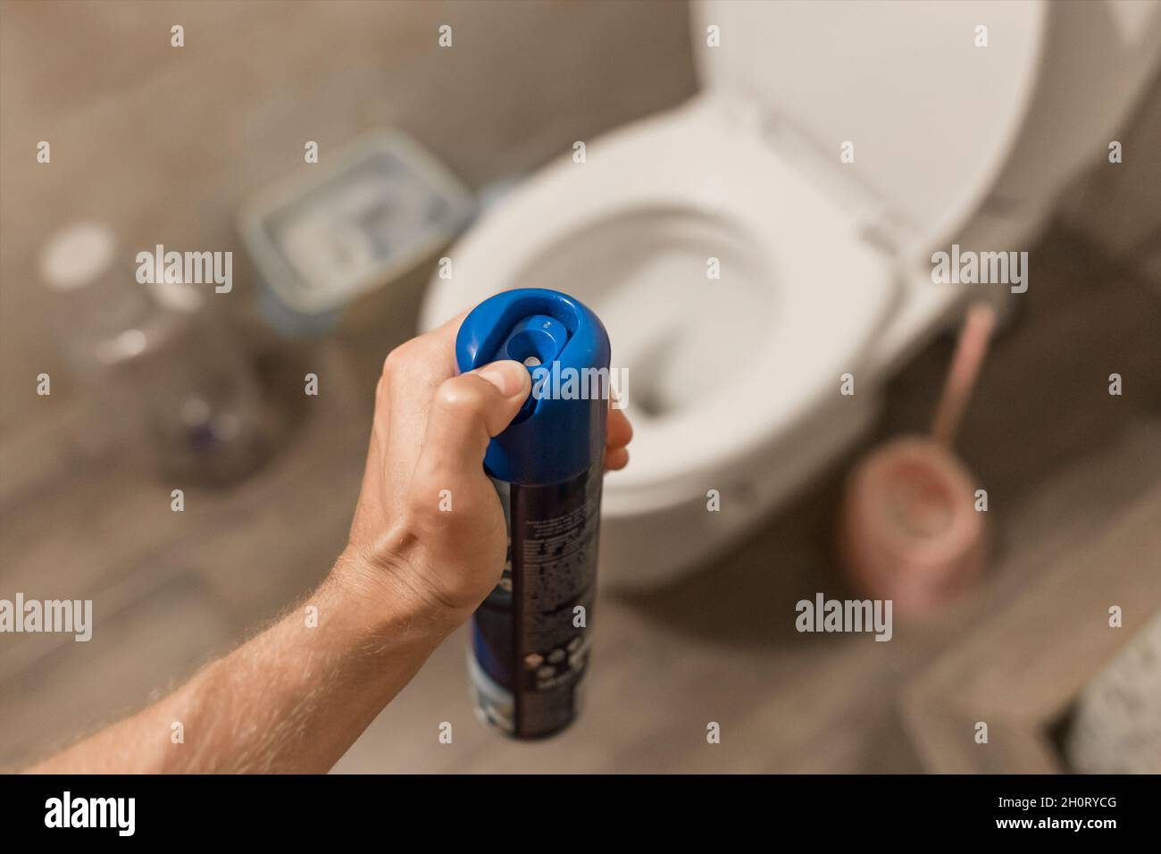 The guy's hand holds and sprays the air freshener in the toilet or bathroom. Home Hygiene Concept. Stock Photo