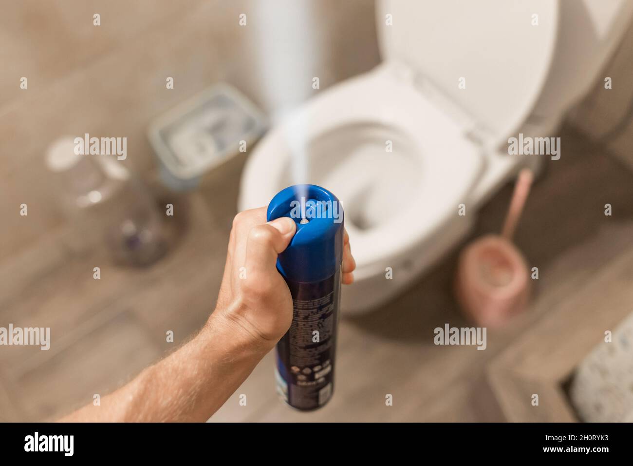 The guy's hand holds and sprays the air freshener in the toilet or bathroom. Home Hygiene Concept. Stock Photo