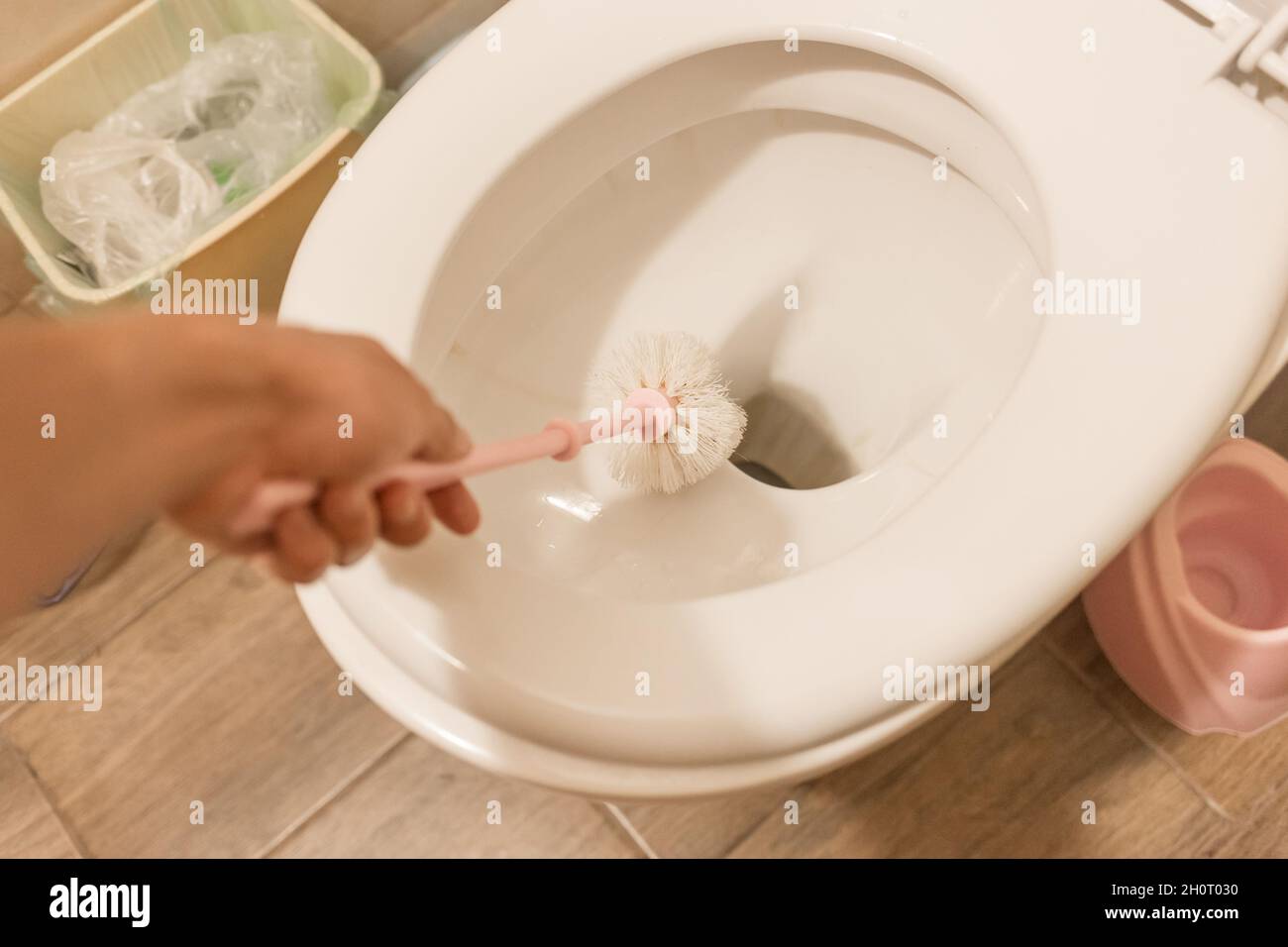 The guy's hand holds the toilet brush and cleans the toilet. The