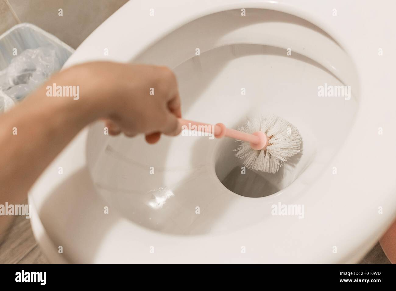 The guy's hand holds the toilet brush and cleans the toilet. The