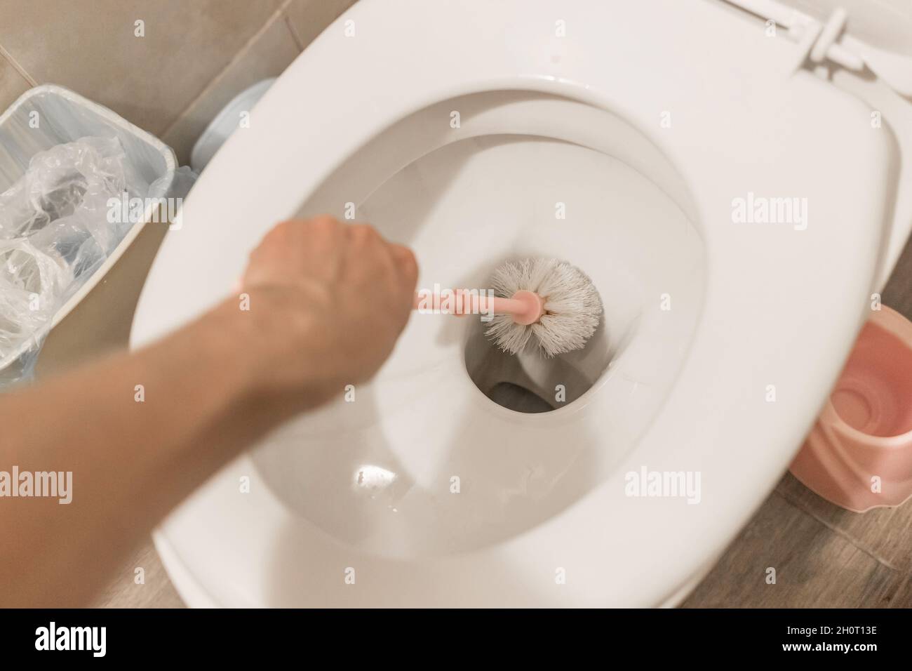 The guy's hand holds the toilet brush and cleans the toilet. The