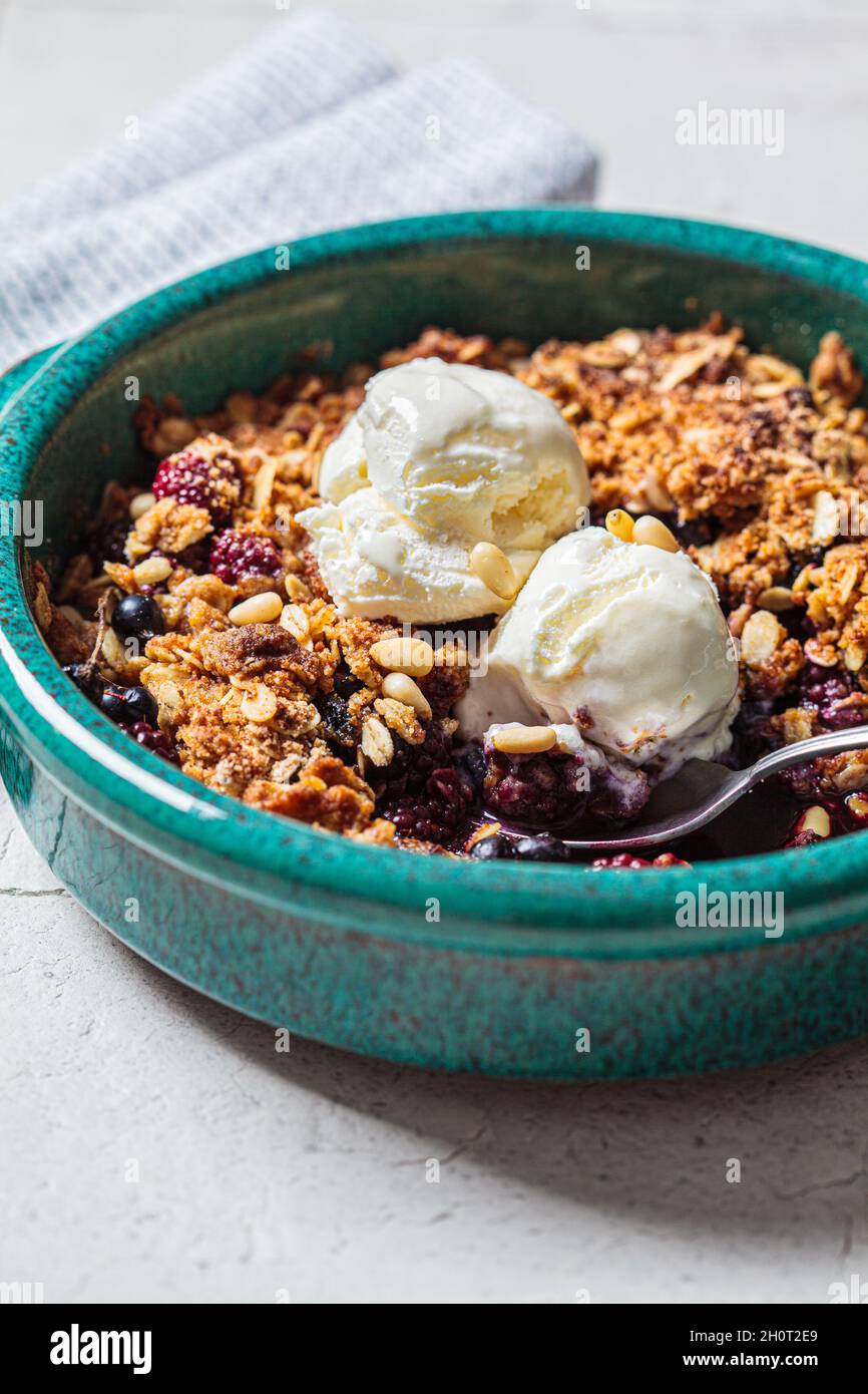 Berry crumble pie with ice cream in blue baking dish, gray tile background, close-up. Stock Photo
