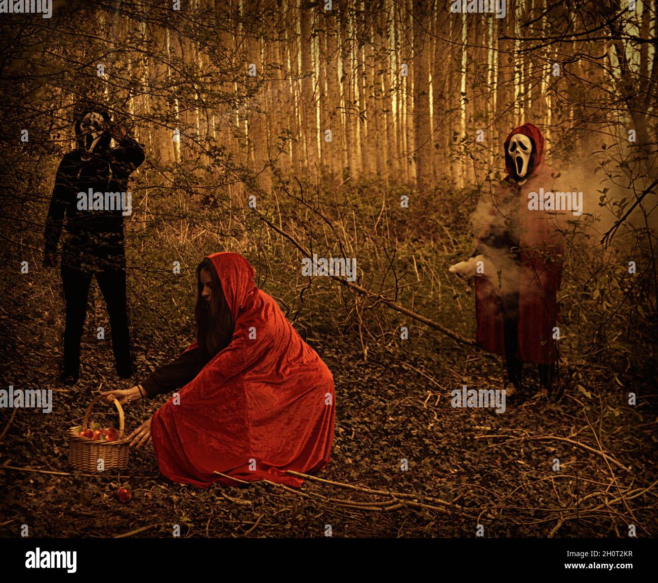 Little red riding Hood with masked person in black standing behind. Shot in shady woodland. Stock Photo